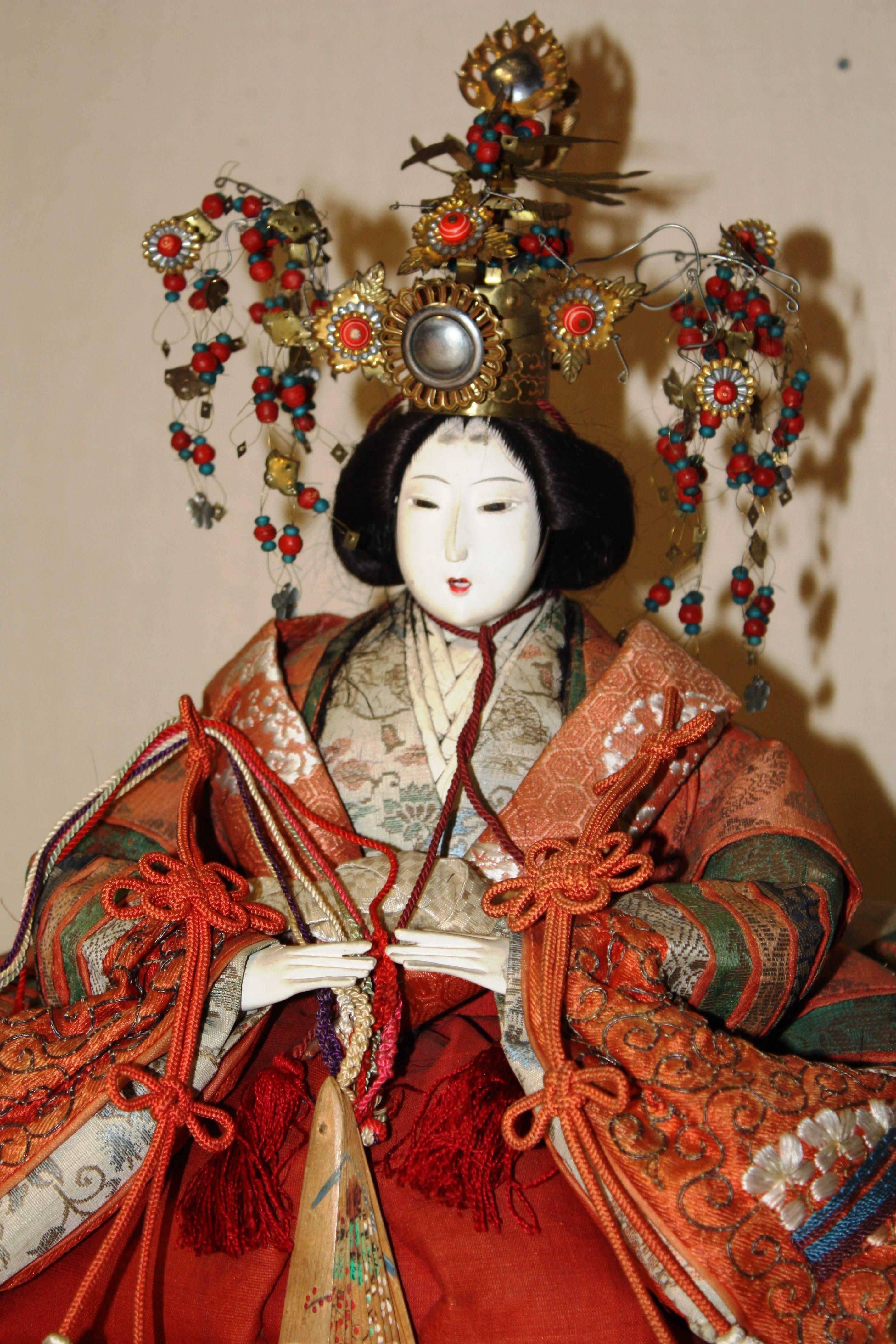 A Meiji Period Japanese doll depicting the Empress with elaborate head-dress, and wearing period clothing, 19th century. The face and hands glazed with crushed oyster shells (Gofun) to create the bright white finish.