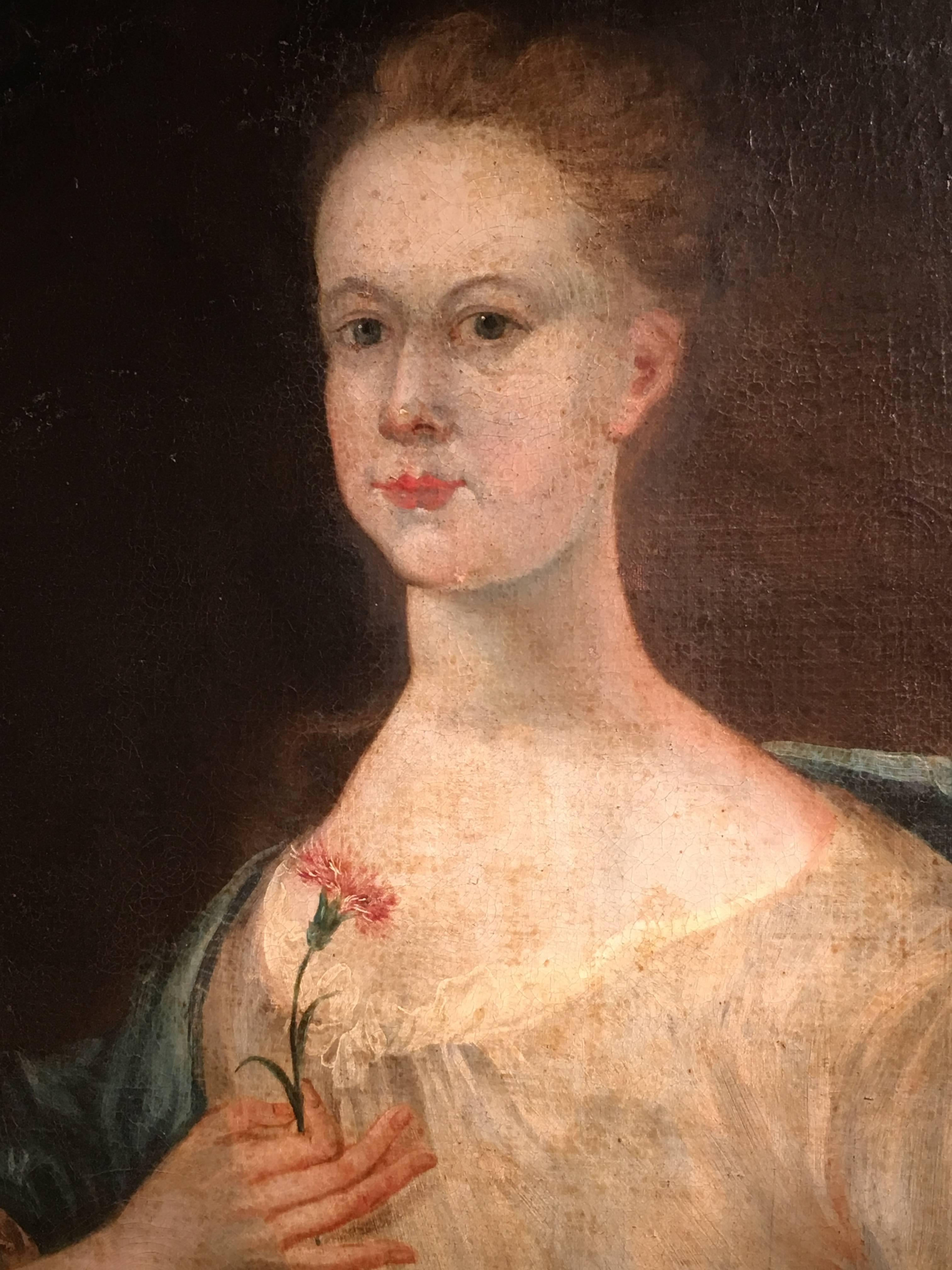 A charming American or English oil-on-canvas portrait of a young woman in a white dress with blue cape holding a flower, with her age (13 years) painted at the top right of the canvas. Later frame.