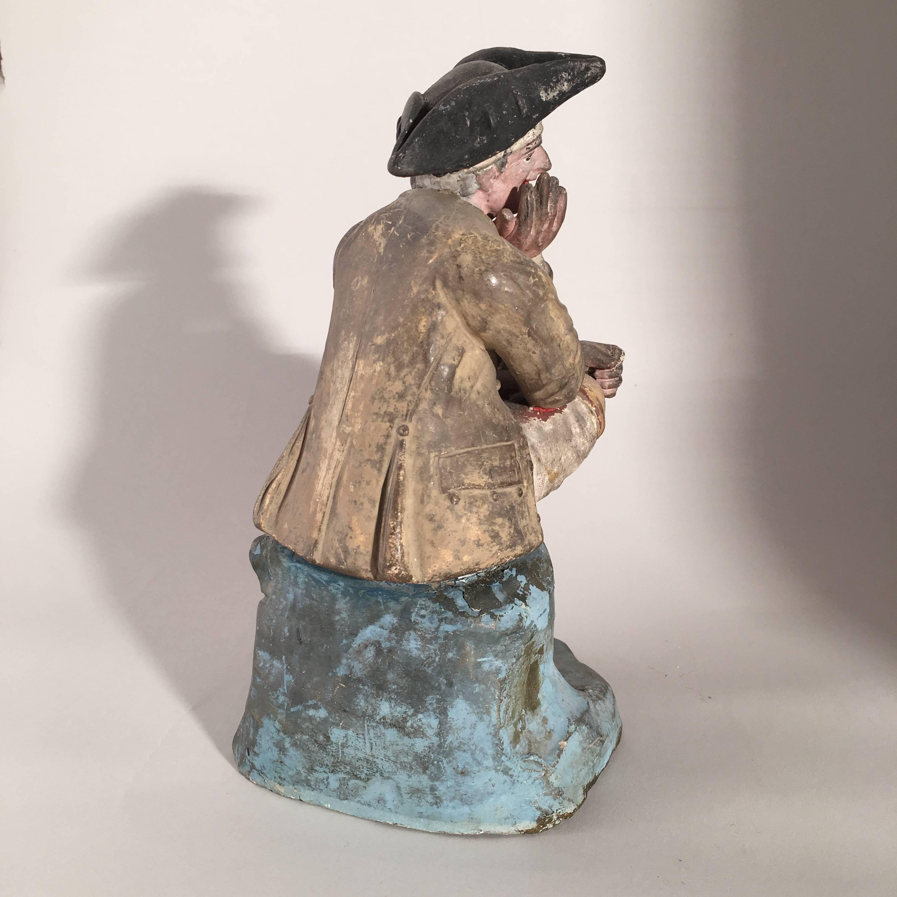 A late 18th century French Provincial figurine of a seated gardener with watering can, in period costume with tricorn hat, circa 1770, in painted terracotta. From the estate of Pierre Moulin, author of French Country style books and founder of