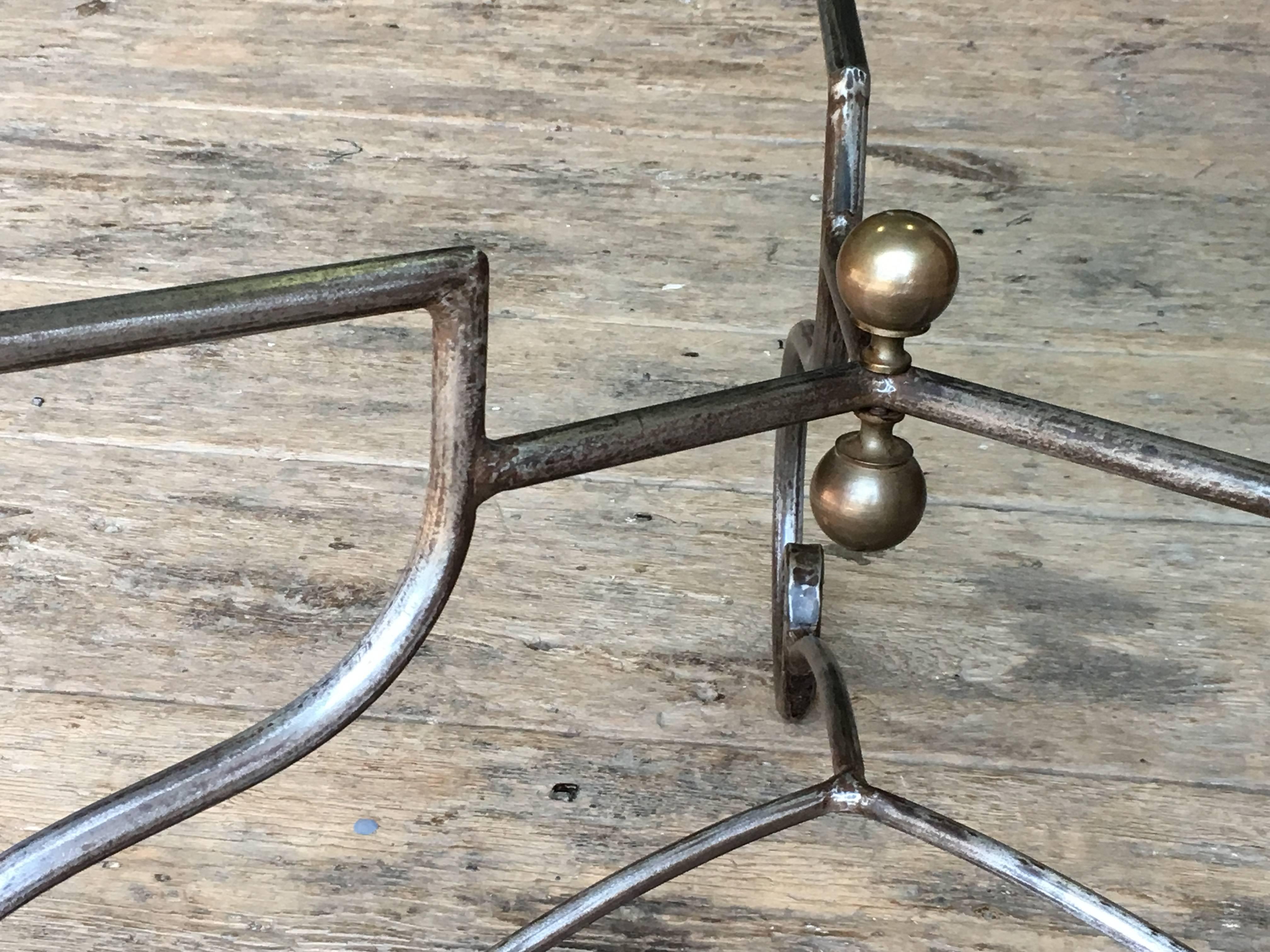 A nicely made wrought iron circular center table / dining table with heavy glass top and brass ball detail, retailed by Pierre Deux in the 1980's. Beautifully hand-forged in heavy steel, wire brushed finish. Tempered glass top.