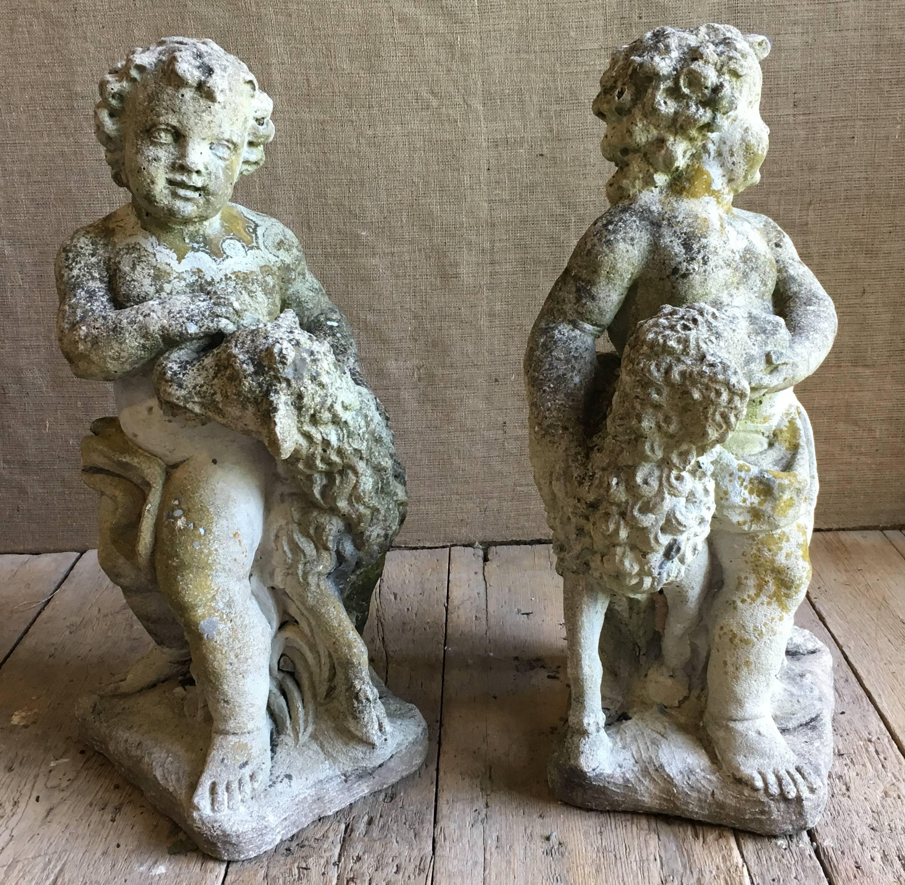A charming pair of life-size garden statues in cast stone, early 20th century, depicting two putti with lambs, each statue facing in the opposite direction to create a true pair. Nice patina with traces of lichen and moss.