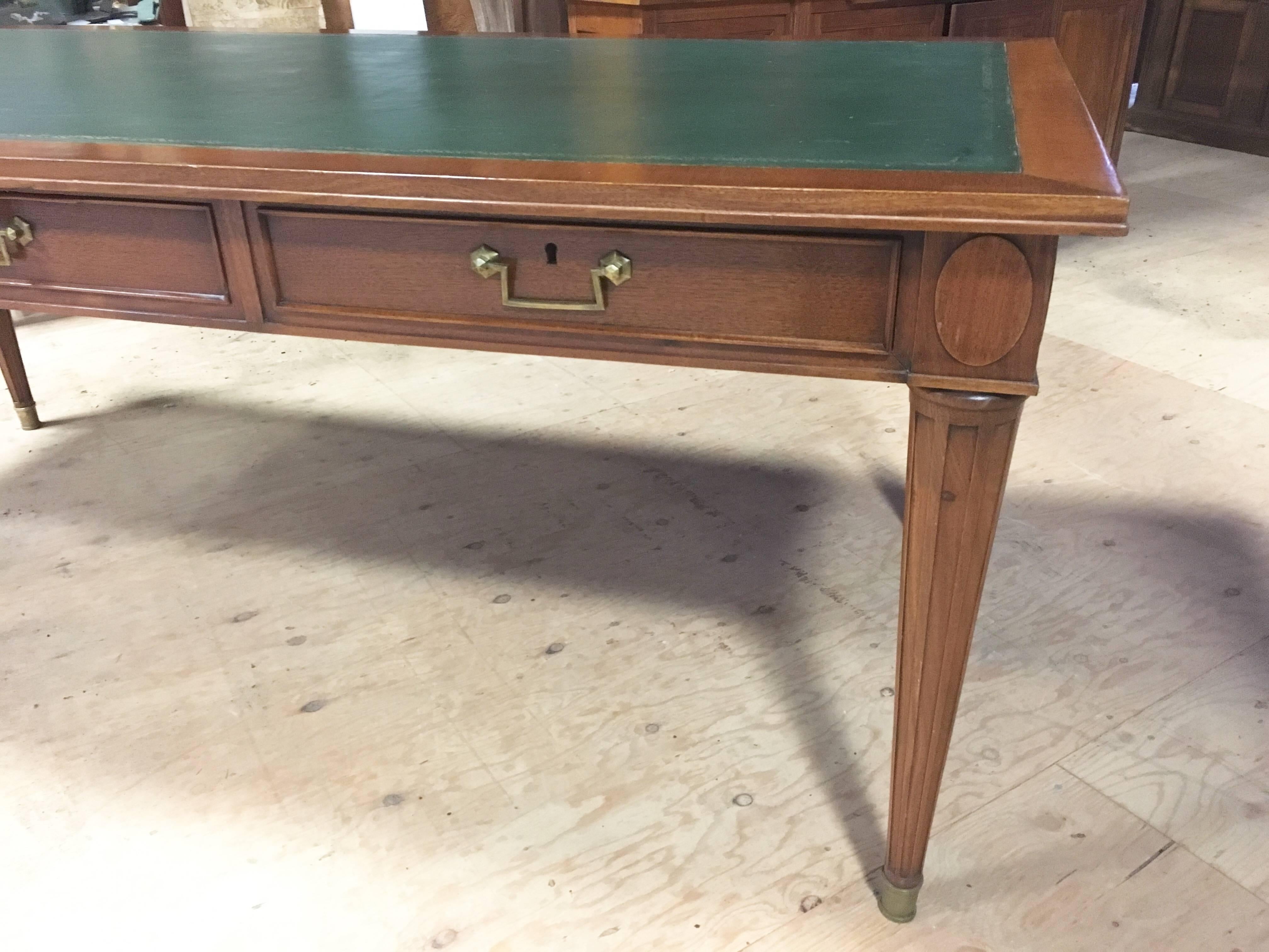 A Classic Louis XVI style bureau plat (writing table) in light mahogany with inset green leather writing surface and three large drawers in the apron. Signed with a metal label in one drawer 