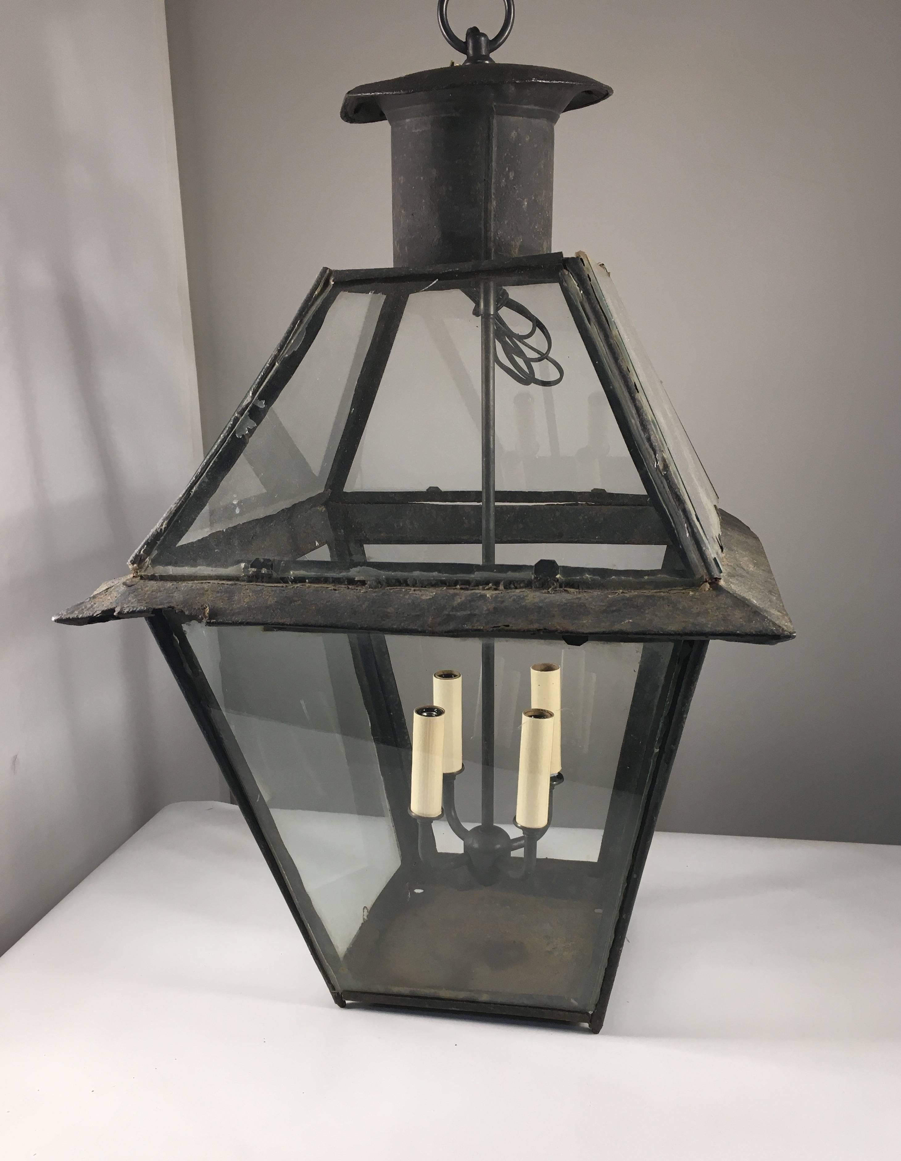 A well-worn 18th century tole hanging lantern, French, circa 1780, with glass panels on sides and top, now wired with a 4 candle cluster suspended inside.