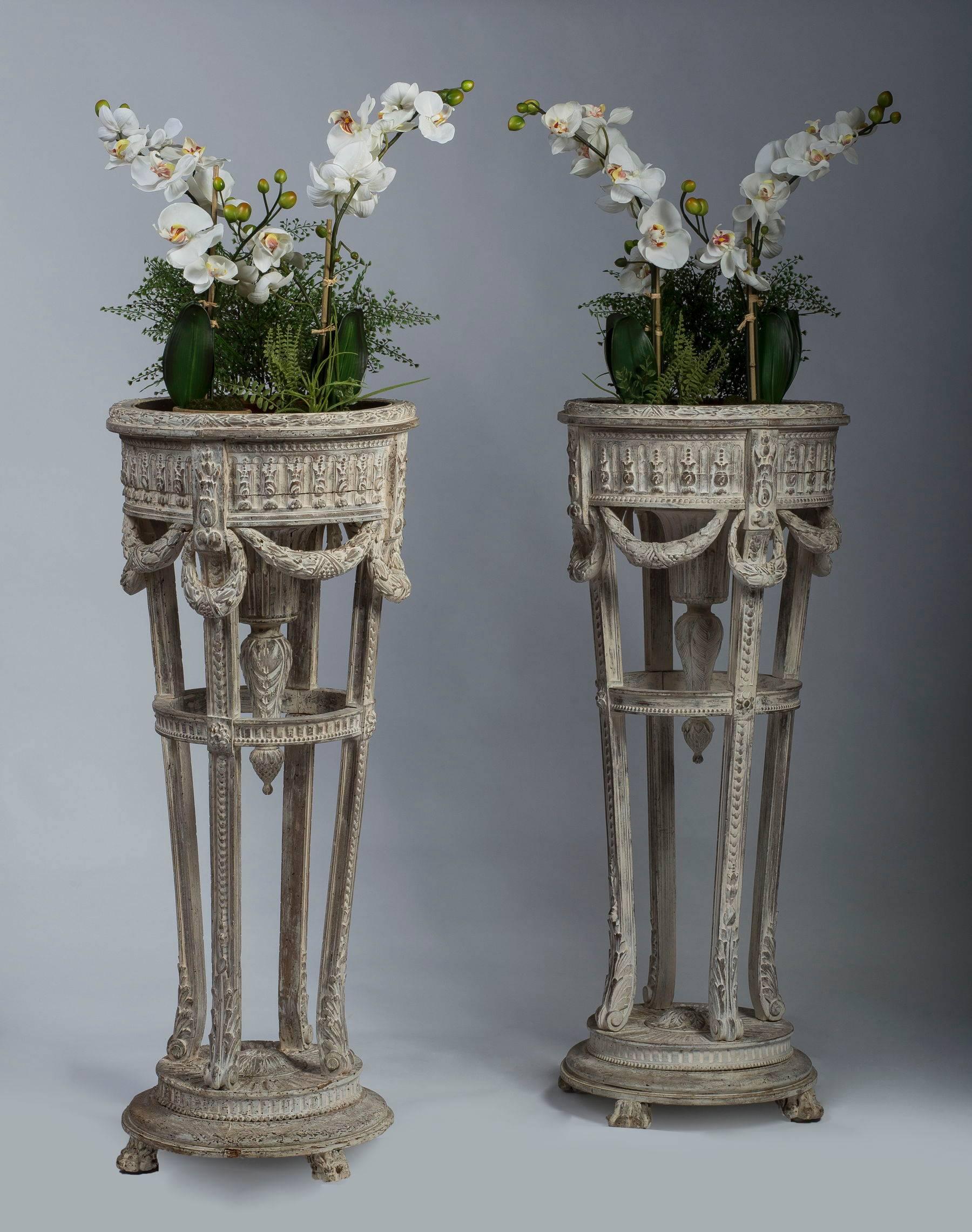 The circular container carved with pearls and rinceaux and supported by an inswept strung-piaster quadripartite stand with a central finial and hung with swags raised on a conforming plinth. This stunning pair is very much evocative of the designs