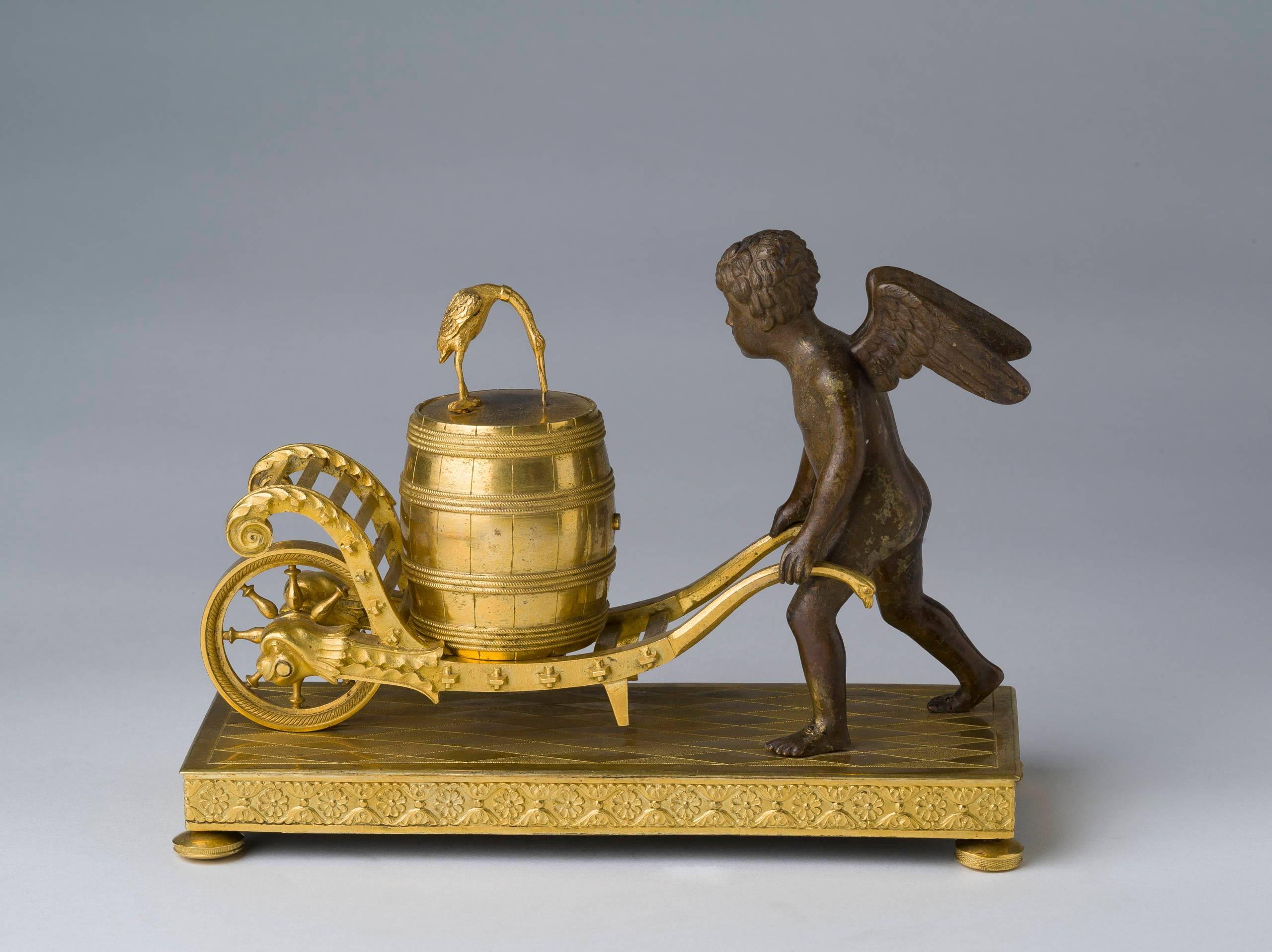 In the form of a putto with a wheel barrow carrying a keg mounted with a clock face topped by a crane, on a rectangular chased plinth ending in bun feet.