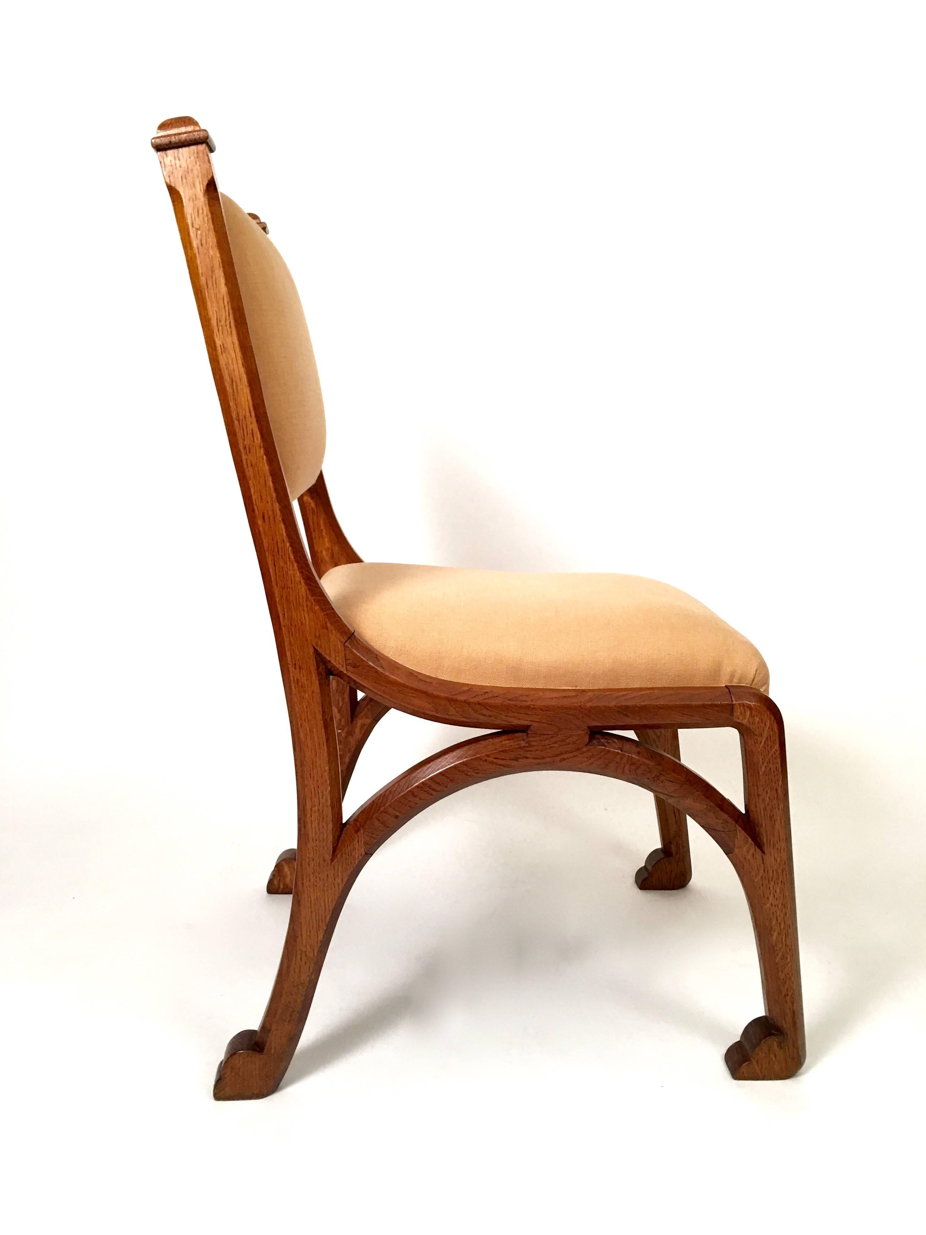 An English Arts and Crafts period Gothic Revival upholstered chair in carved oak, in the manner of A.W.N. Pugin, with wonderful lines, the square section supports and legs all sinuously joined and terminating in stylized backward facing animal paw