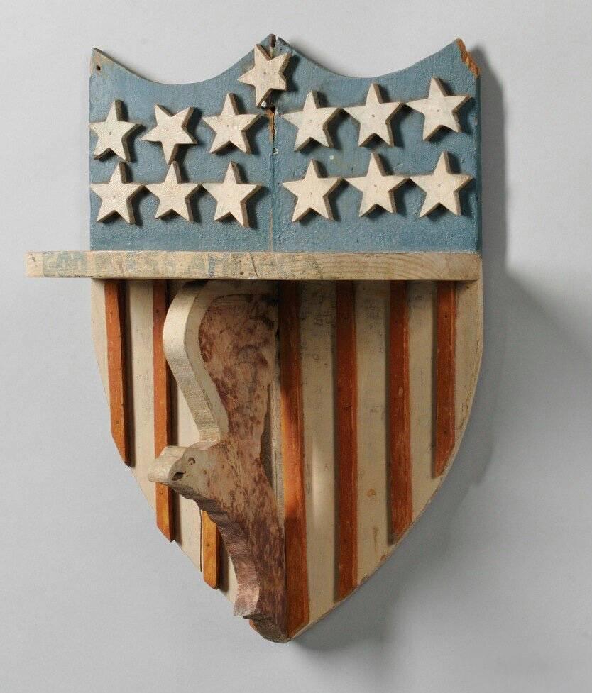 A patriotic American Folk Art bracket shelf, the shield shaped back with applied painted carved wood stars and stripes, the semicircular shelf with 