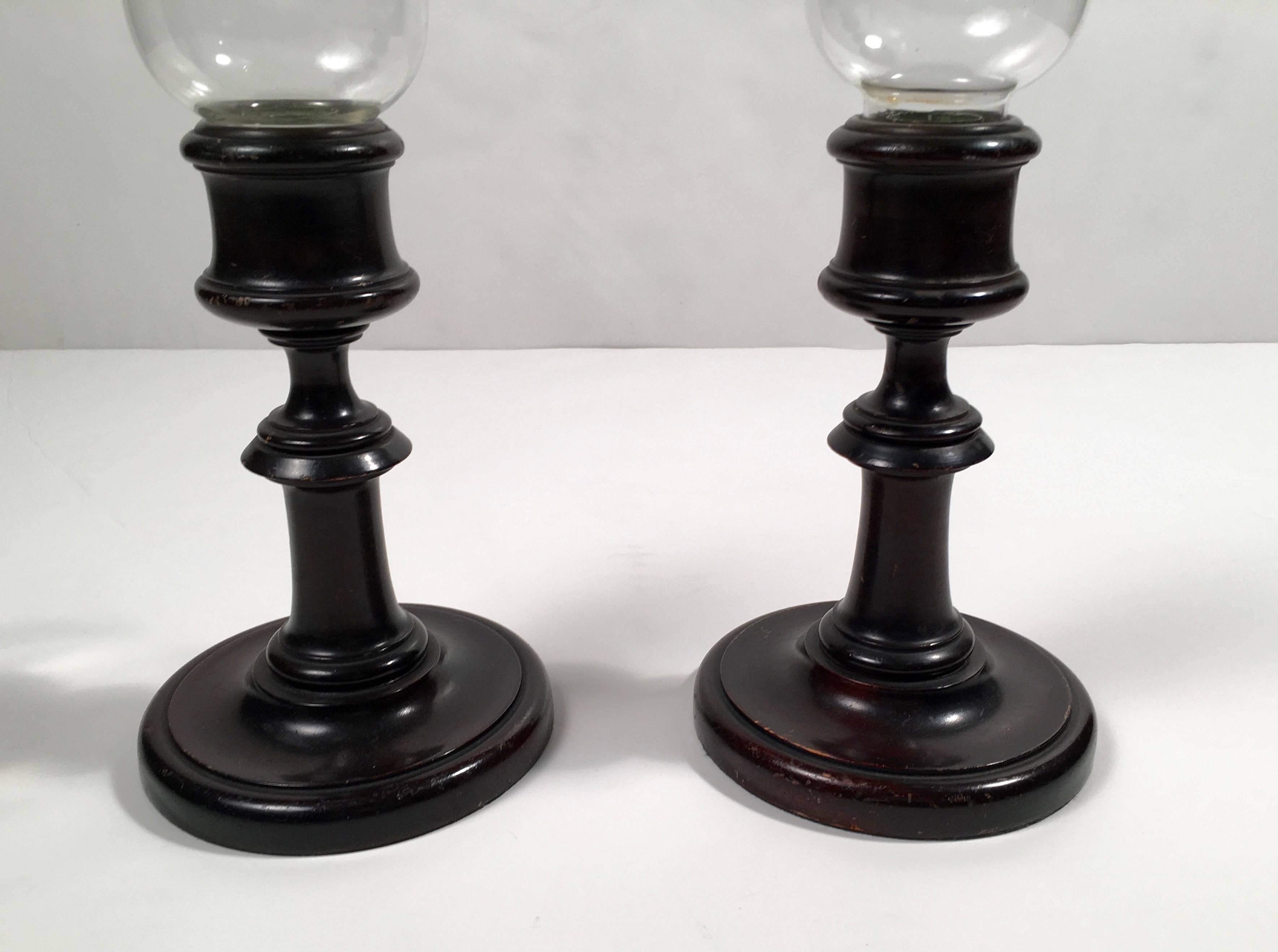 A pair of ebonized turned solid mahogany candlesticks, the removable, inverted bell shaped glass hurricane shades etched with grapes and vines, the underside of the bases with old green felt, one retaining its original Wanamaker's store label: 
