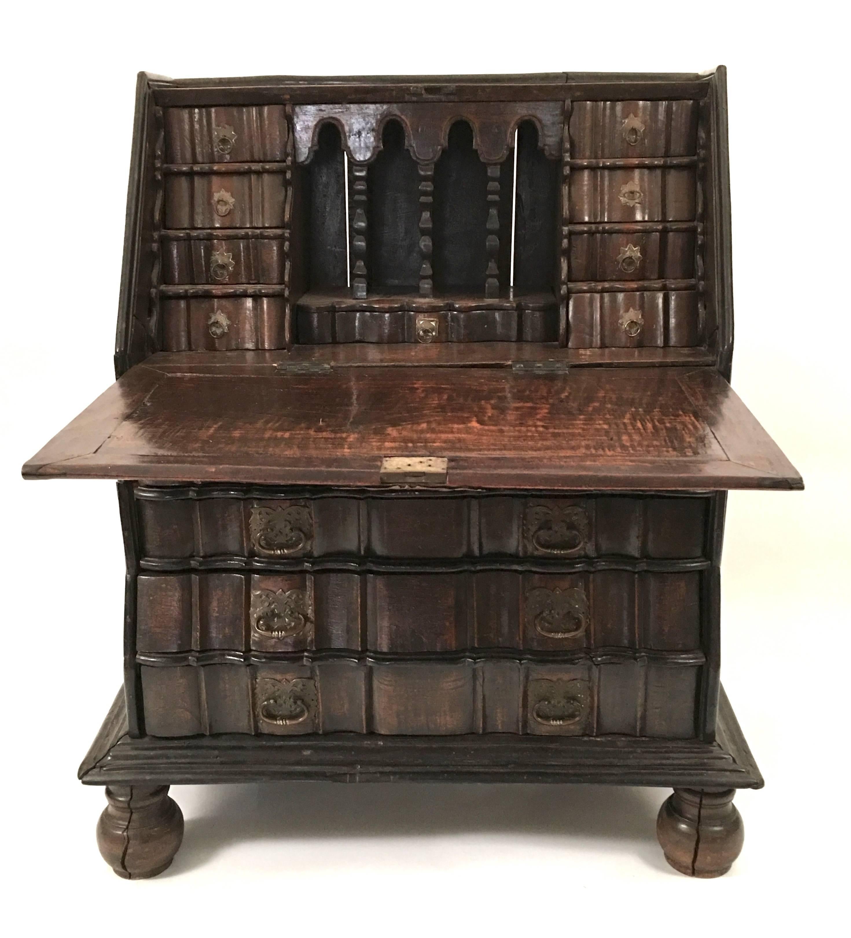 An unusual and sculptural block fronted Dutch Colonial slant lid desk in padouk wood with pierced metal drawer pulls and bird-decorated escutcheon, the exterior of the case with channeled carved top and sides, the fall front writing surface