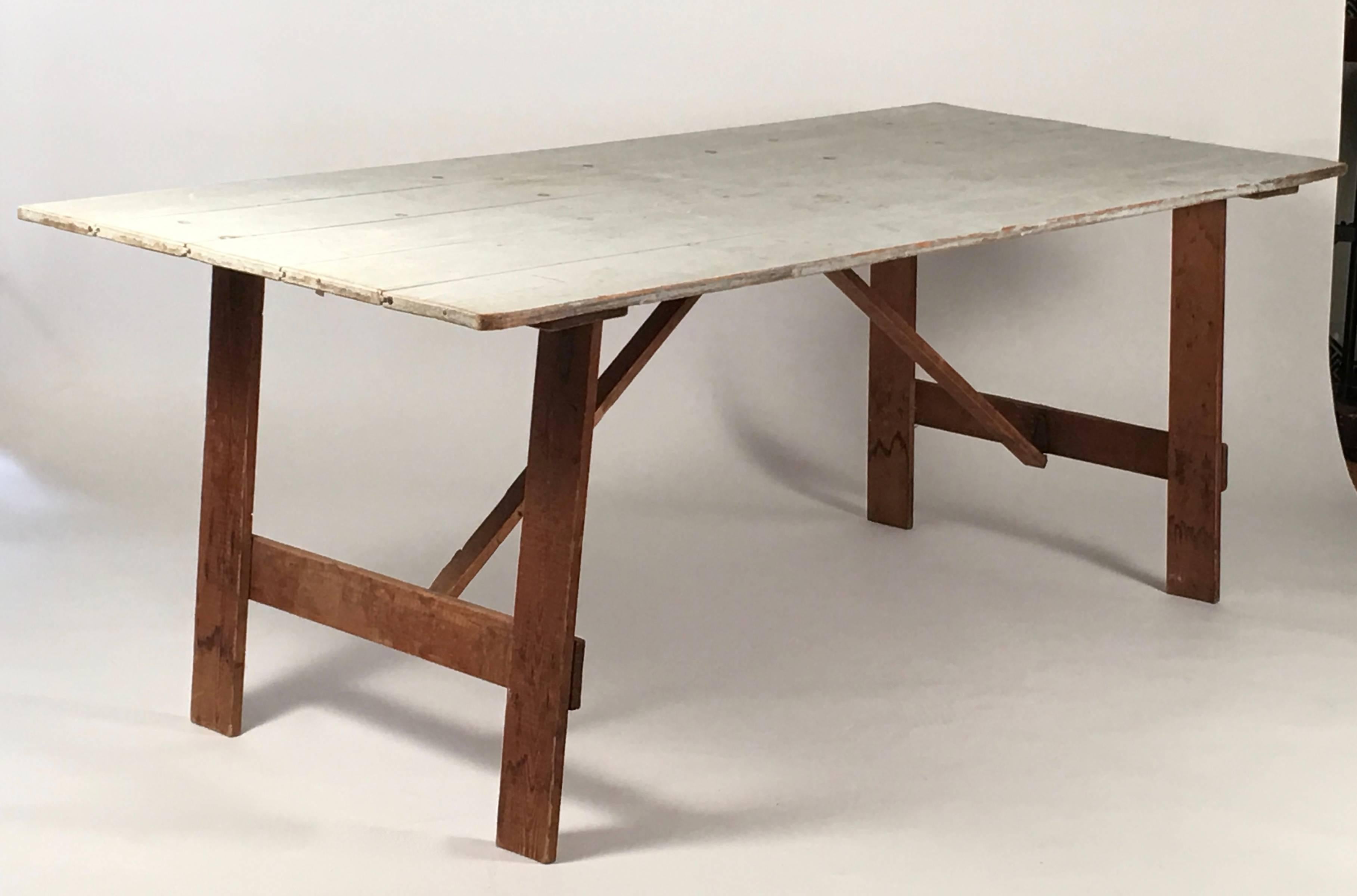 A country folding trestle clam bake table, the top made with wood boards in beautiful old light blue paint, over four legs joined by cross stretchers and further reinforced with diagonal cross stretchers, all of which are hinged and fold to make the