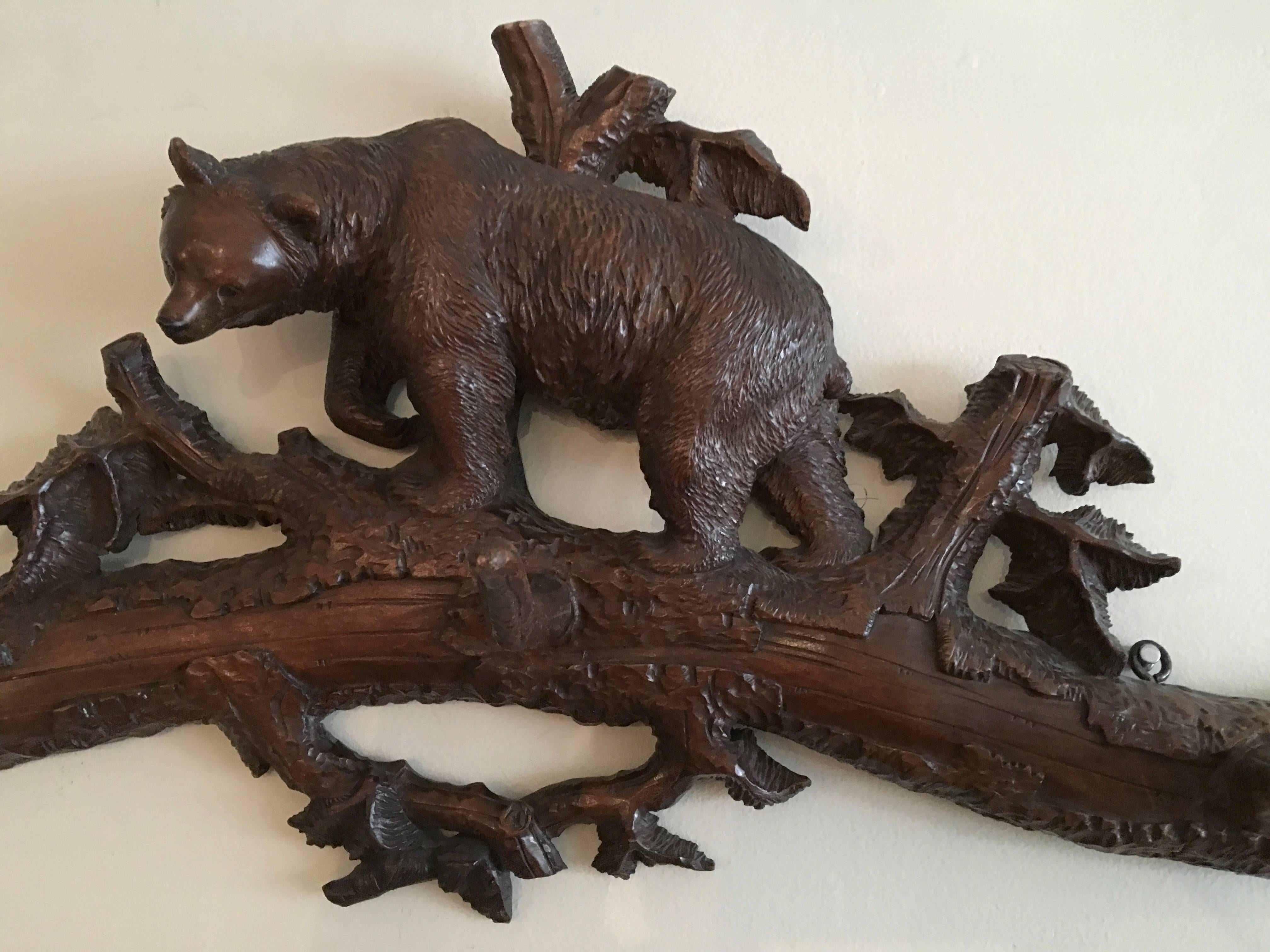 A black forest carved walnut hat and coat rack with beautifully and naturalistically carved bear walking across a well carved log and tree branches, with 3 long, sturdy antler-like hooks for hanging hats and coats.

With a gift inscription in