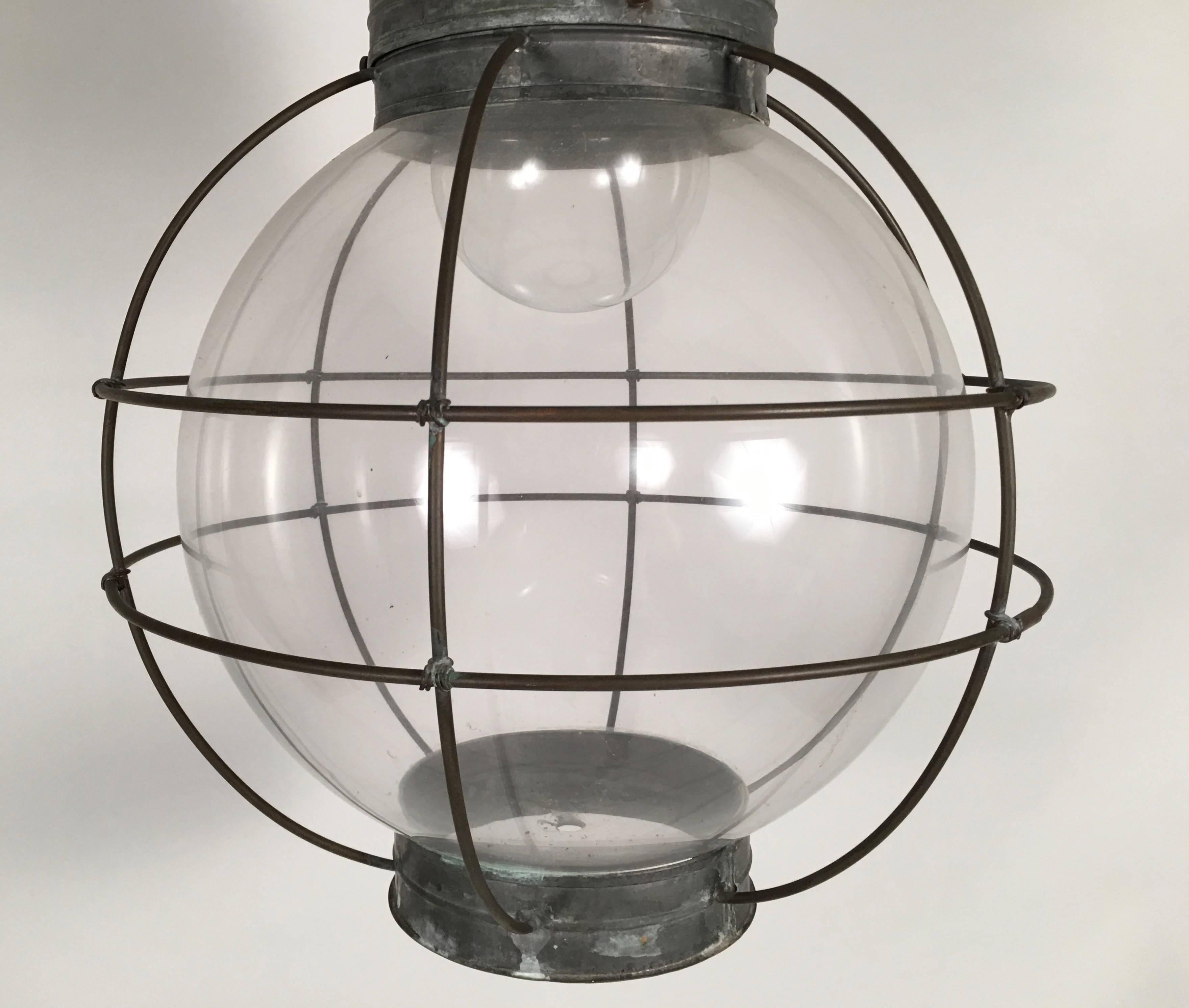 An unusual oversized nautical onion lantern in tin and blown glass, newly rewired, the conical tin roof over a tin collar punched with stars for venting heat, over a blown glass sphere within a tin cage to protect from breakage.

This form dates