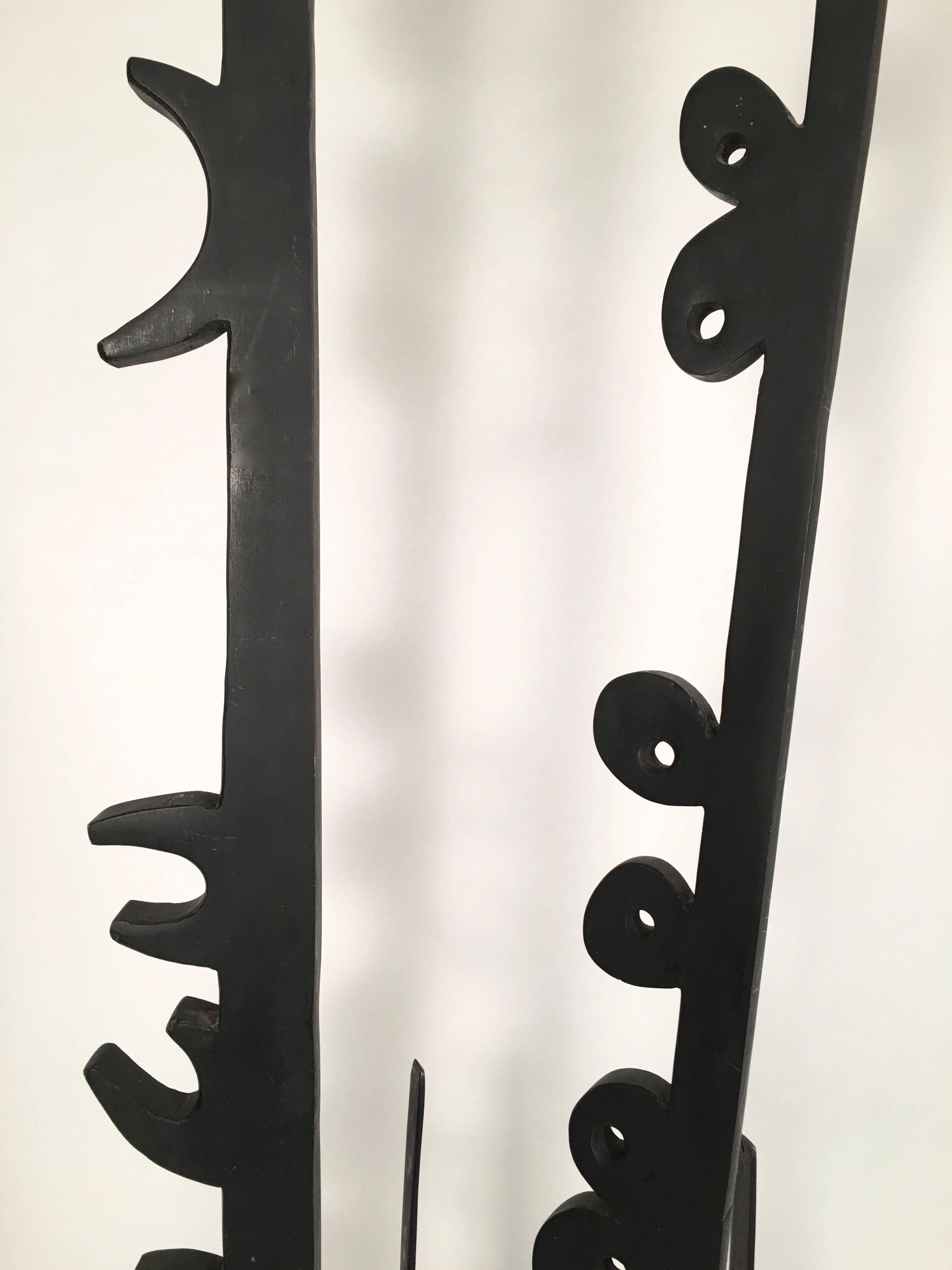 A tall, striking mid-century modern sculpture, evocative of the work of Louise Nevelson and African, primitivist modern art, in black painted metal, comprised of ten vertical forms of various sizes, the two tallest with C like shapes and circular