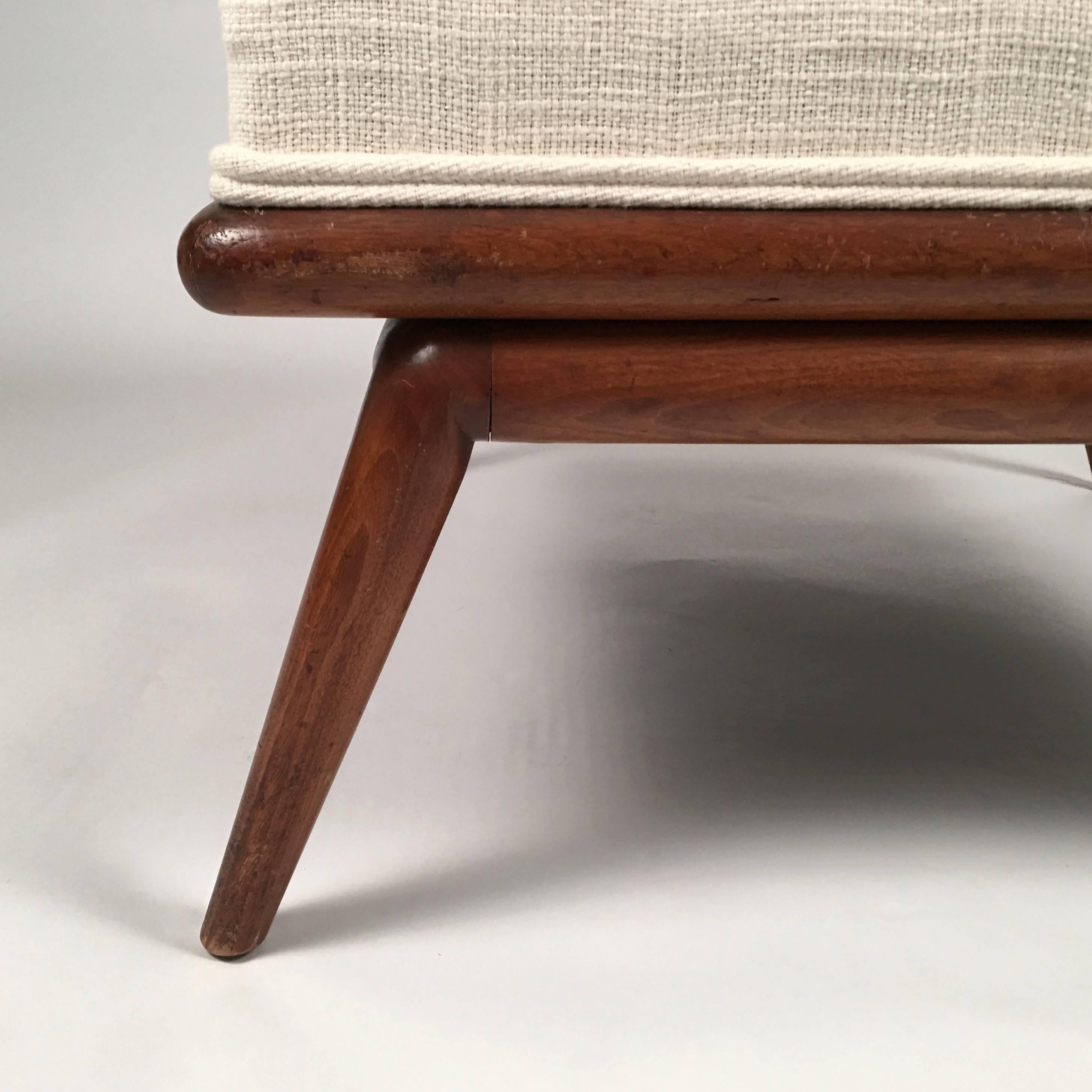 A  beautifully made mid-century modern upholstered square ottoman with angled cylindrical carved walnut legs, designed by T.H. Robsjohn-Gibbings and made by Widdicomb, Grand Rapids, Michigan, circa, 1950. Characteristic blend of classical form and
