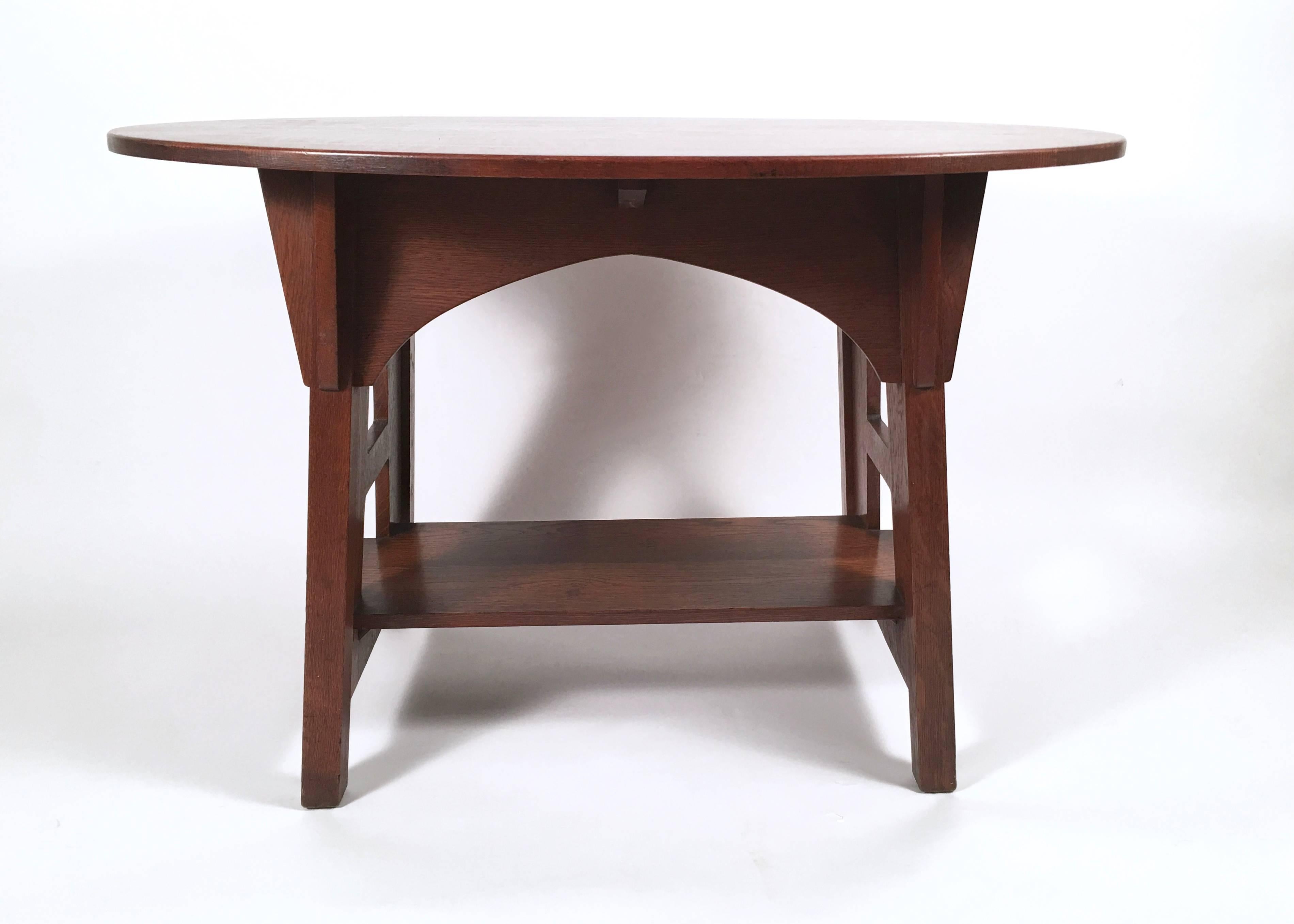 An Arts & Crafts period library table by Charles Limbert, No. 146, the oval top with lively figured boards of quarter sawn oak over an arcaded apron with bracket supports, flanked by trestle supports with square cut outs (influenced by the Viennese