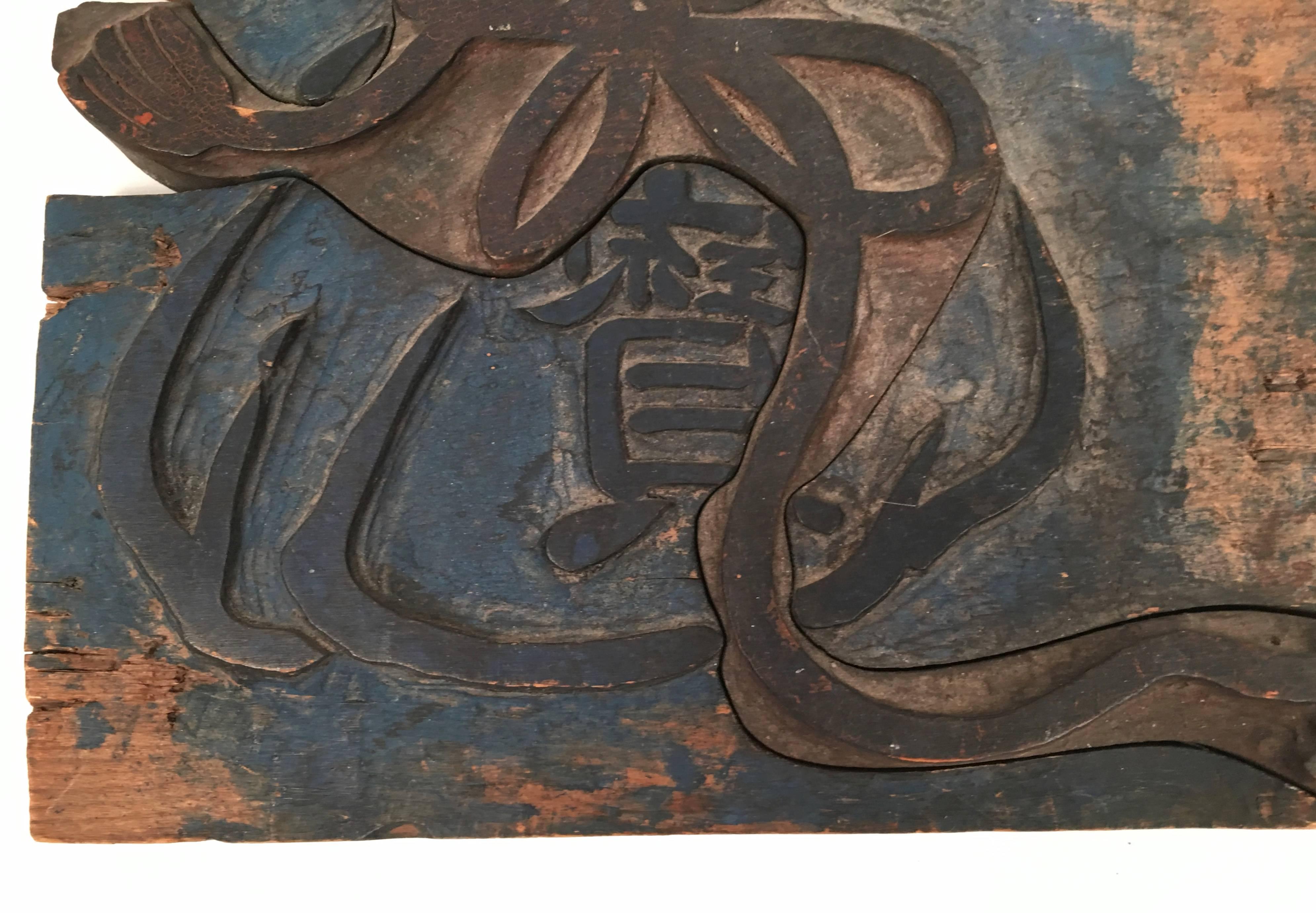 An antique Chinese printer's wood block, carved with the character 'bao,' meaning 'precious,' playfully centered within a ribbon tied cloth sack, suggesting that the contents are valuable. The square block is carved in two interlocking sections and