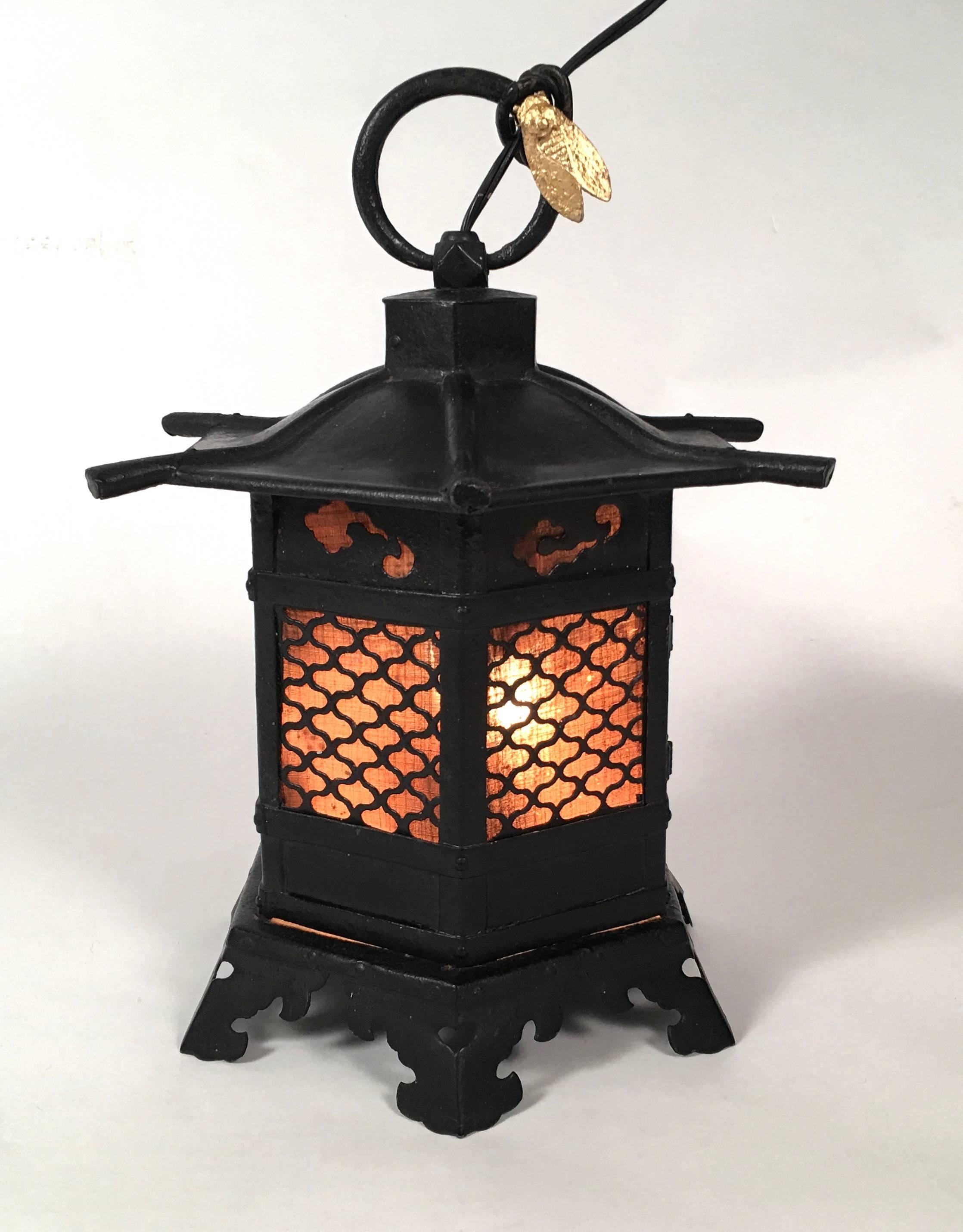 A Japanese wrought iron lantern of pagoda form, the circular hanging ring loop decorated with a cicada, newly gilded, over the grillwork doors backed with original linen and enclosing two lights, raised on bracket feet with cloud scroll decoration.