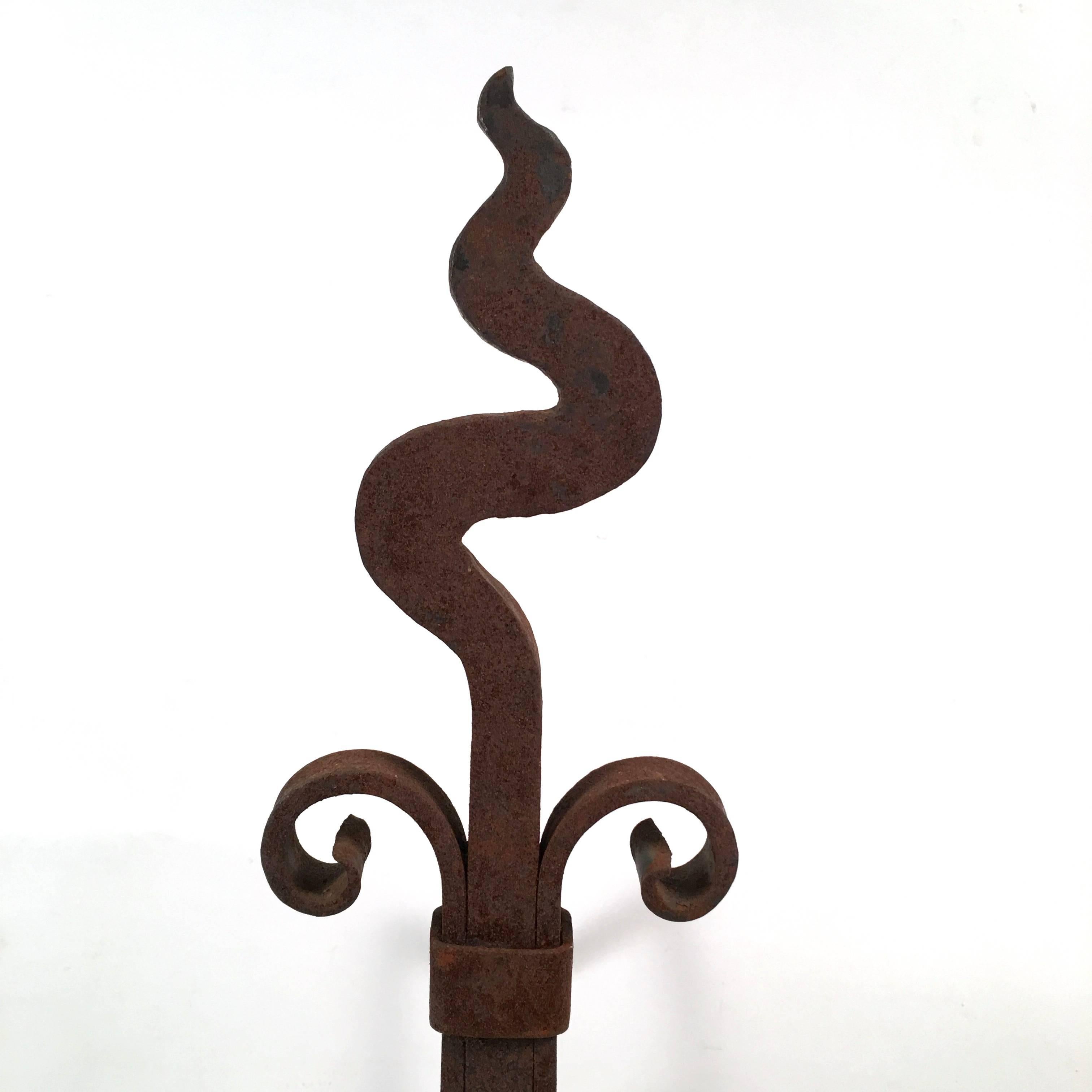 A graphic pair of Pair of Arts and Crafts period wrought iron andirons with wonderful lines, each one with a squiggly, serpentine top over a square section support, the top of which is wrapped with a band from which two scrolled elements issue, all