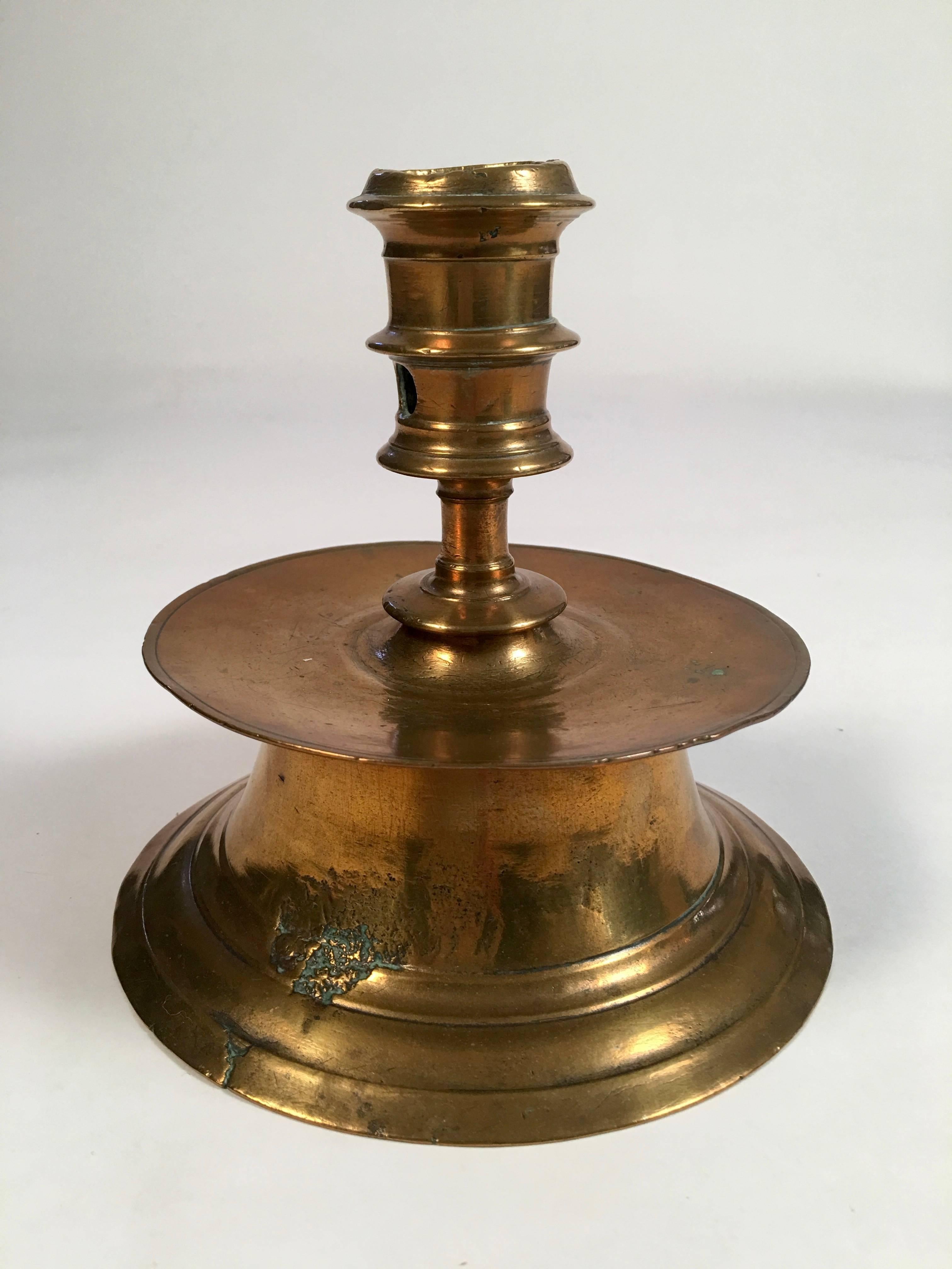 A pair of 17th century (or earlier) European brass capstan candlesticks, the tapered socket with candle stub hole over a wide drip catcher, on a raised spreading circular base. Historic Deerfield Museum accession number P118 painted in red on the