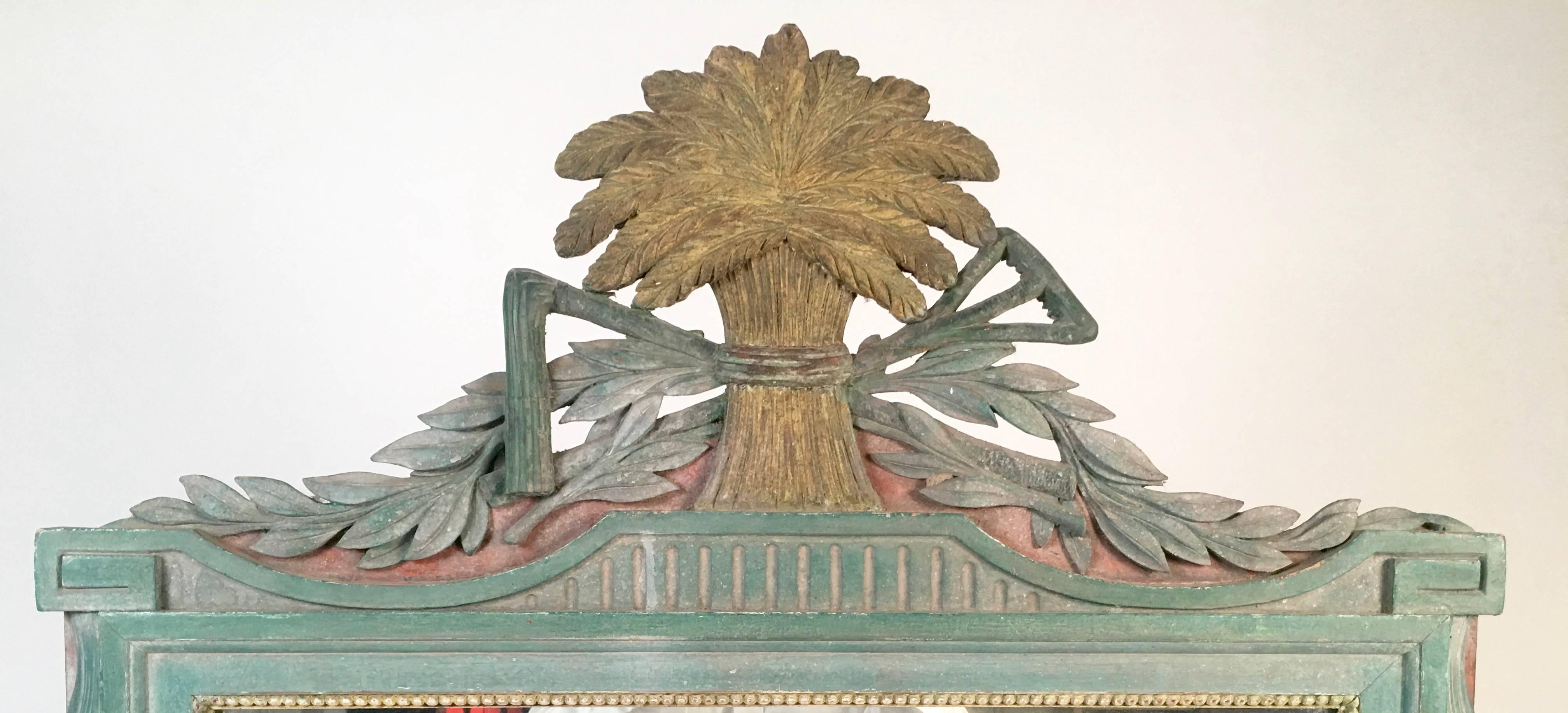 A beautifully carved and painted wood Louis XVI style mirror with agricultural or farming motifs, in tones of muted, wonderfully chalky green, yellow and gold, of rectangular form, the cresting centered by a bound sheaf of wheat flanked by a rake