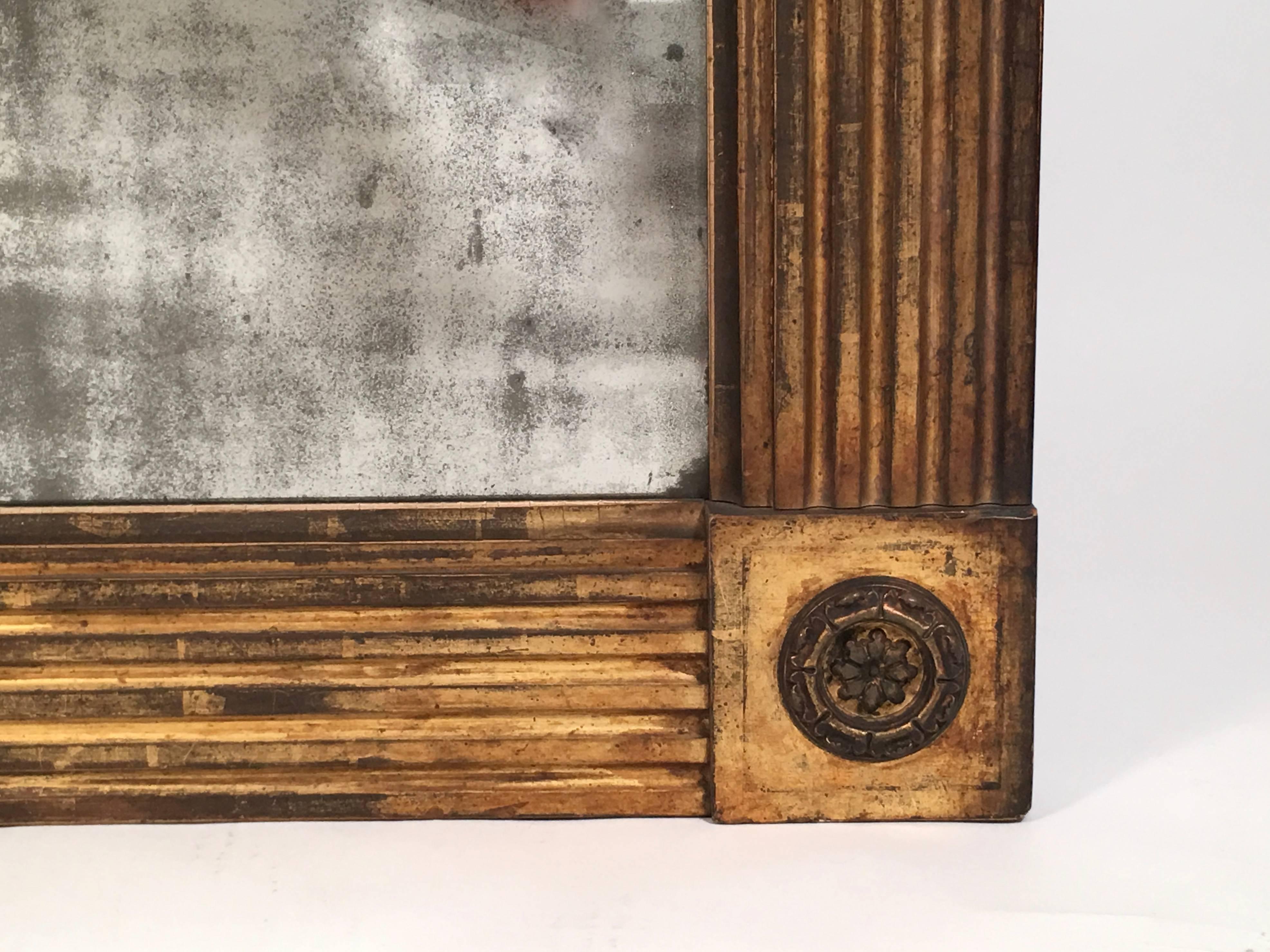An American Classical carved giltwood mirror or rectangular form, possibly Philadelphia, the frame with boldly carved fluting, the corners with raised square ornaments, each centered by an ormolu rosette, retaining its original mirror plate, circa