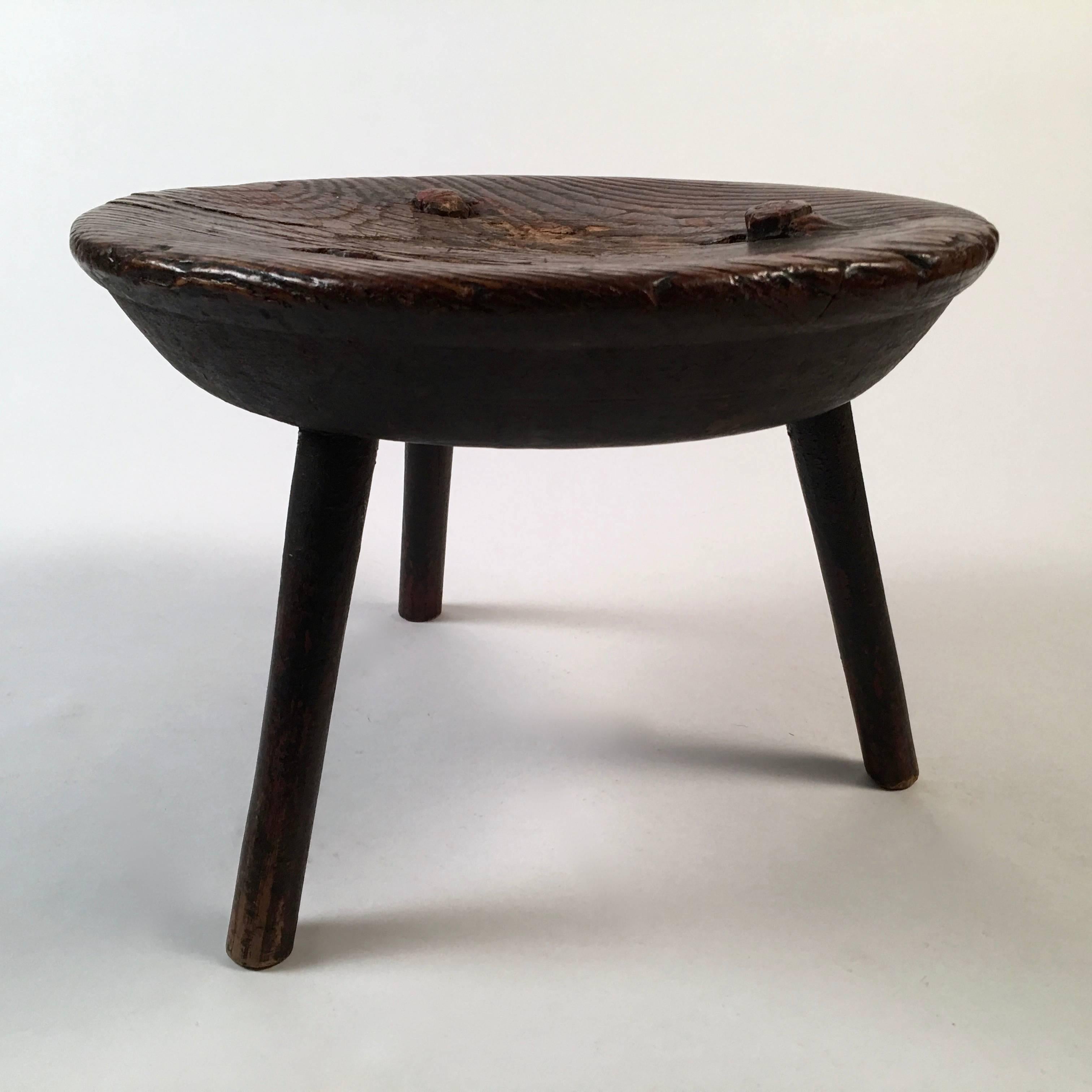 An 18th century round milking stool, with wonderful character, the thick, tapering round solid oak (or elm?) top, retaining traces of old red surface, with 3 spayed circular pegged legs. Great color, texture and patina. Solid and useful as a low