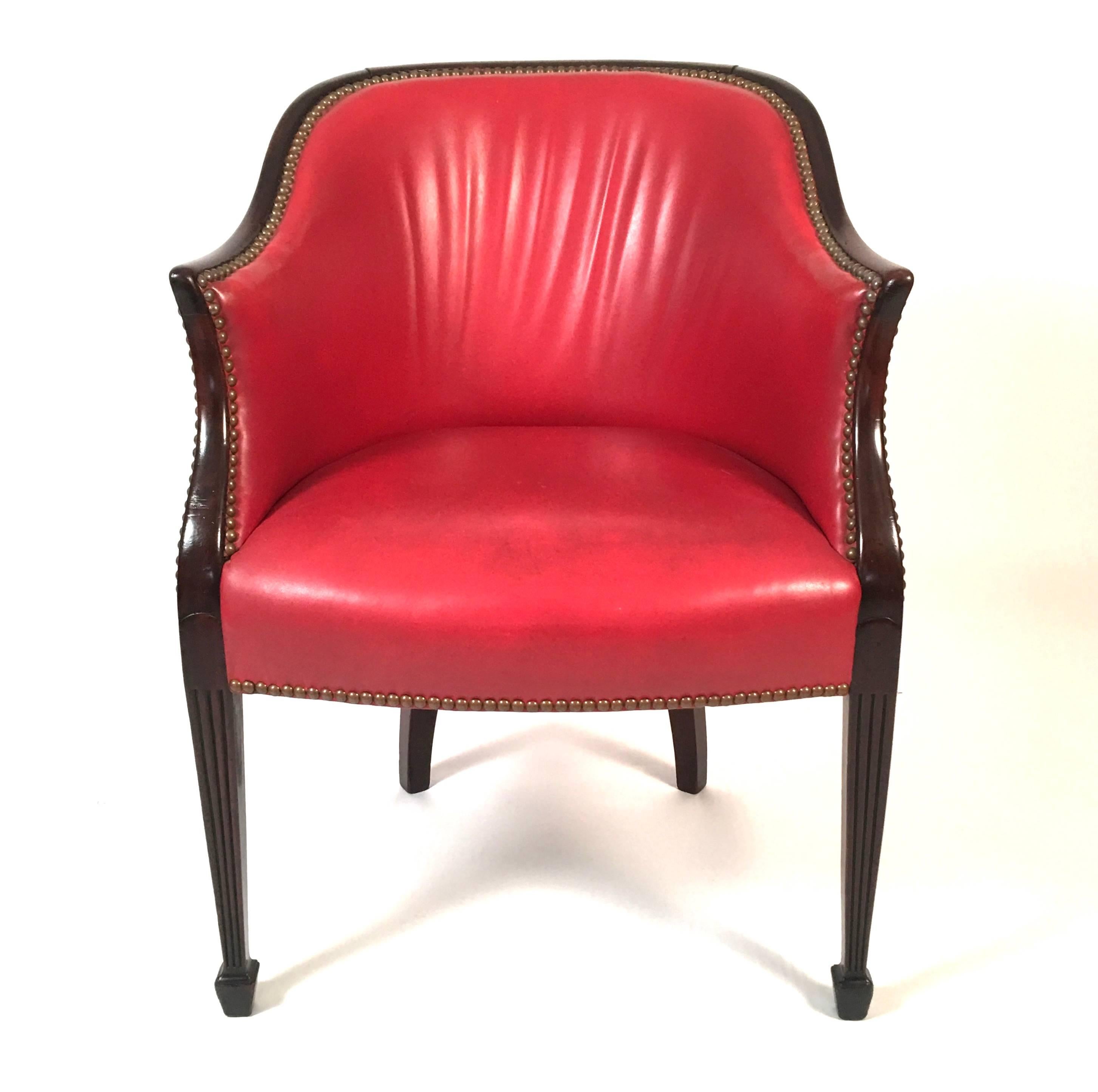 A George III period Hepplewhite barrel back chair in mahogany, upholstered in red leather with decorative brass tacks, the curved back leading to shaped, down swept arms, raised on two carved, fluted tapering square section legs terminating in spade