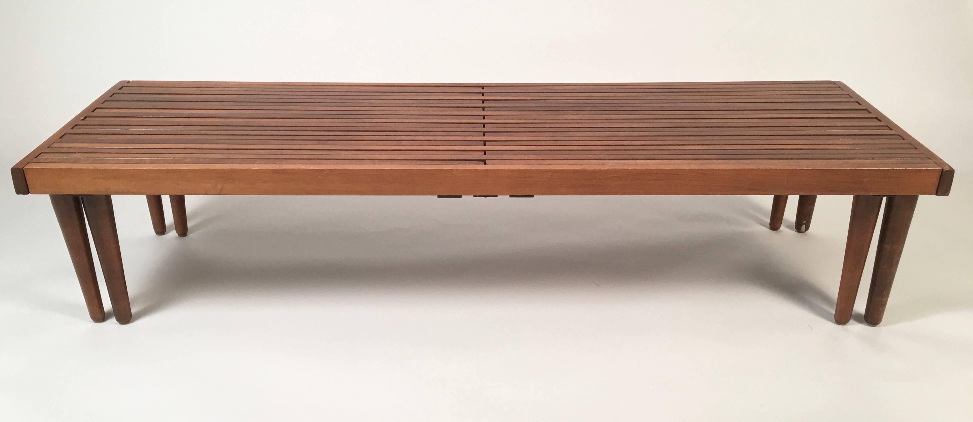 An adjustable length Mid-Century Modern slat wood coffee table or bench which telescopes in and out from a minimum length of 55 1/2 inches to a maximum length of 8 feet, with metal straps underneath the top for added strength, supported by 8