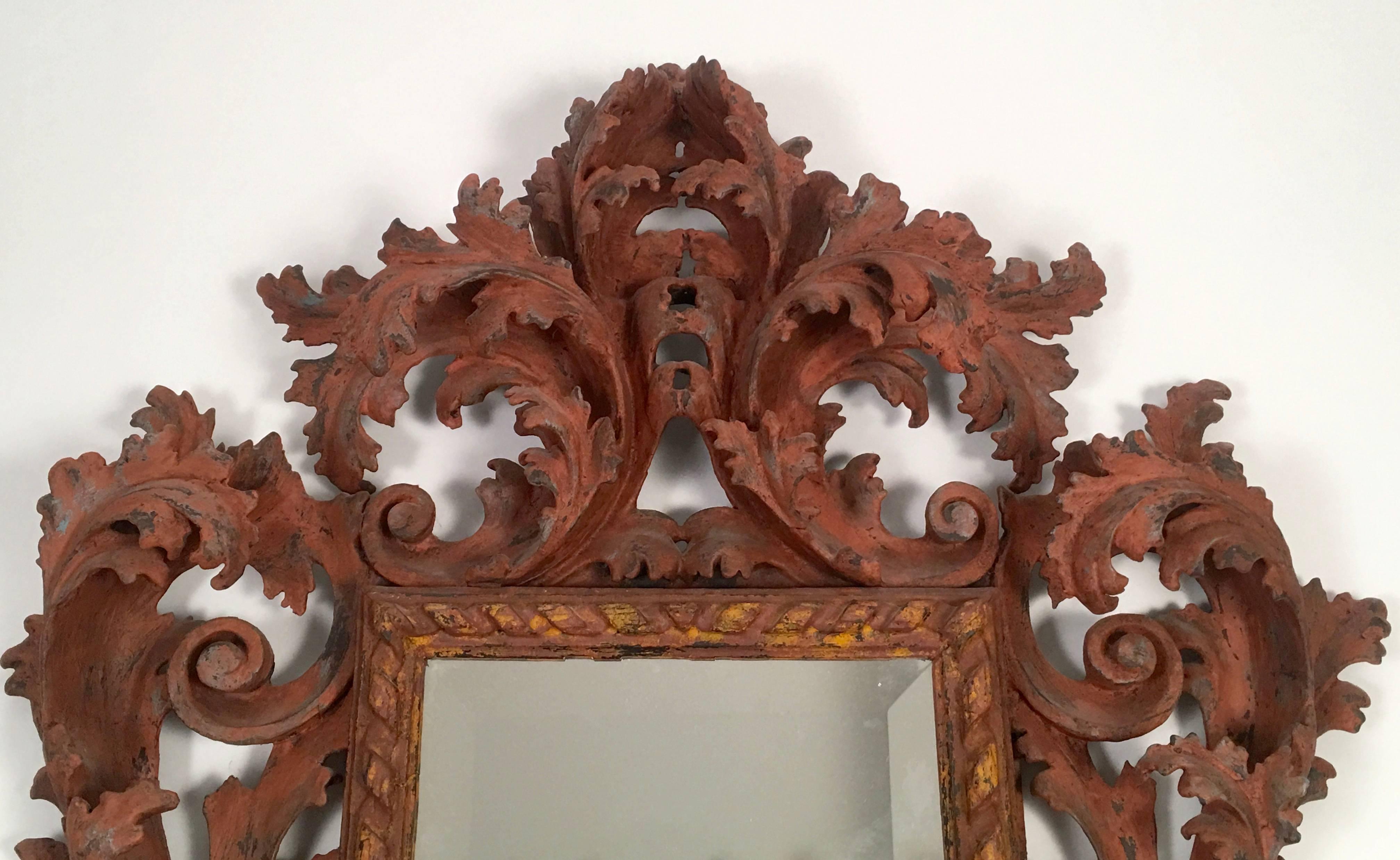 A dramatic and highly decorative Italian Baroque style carved and salmon painted  wood mirror, with boldly carved acanthus leaves and architectural scrolls surrounding a rectangular beveled mirror with highlighted rope twist surround.  