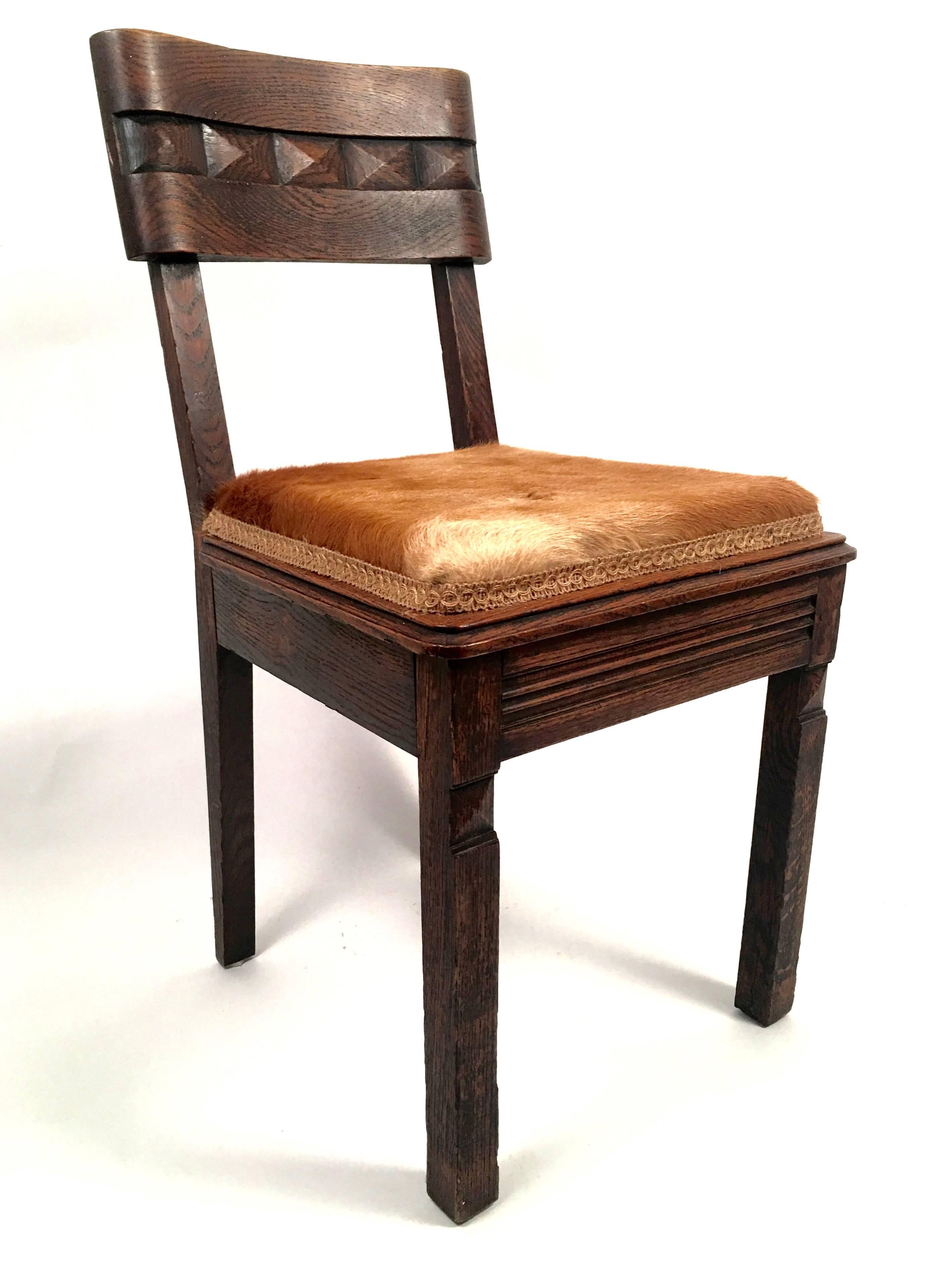 A stylish and well made pair of Art Deco chairs in carved oak, the curved rectangular backs with a band of carved gemstone decoration in the middle of each, the seats upholstered in luxurious deer fur with hemp gimp trim, the seat rail and square