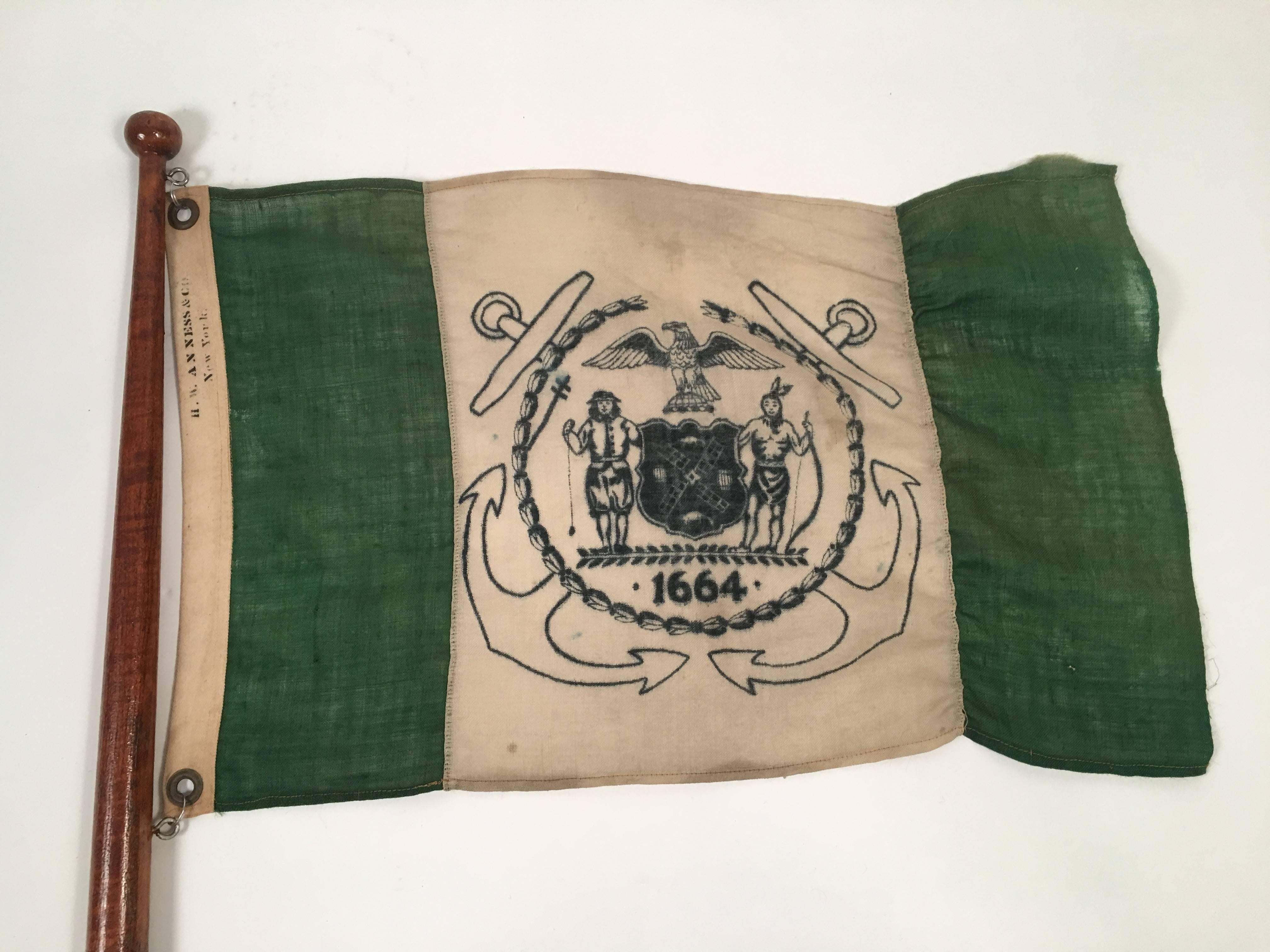 A green and white linen/cotton burgee on a mahogany standard with ball finial, with the seal of New York City printed in blue on white in the middle and flanked by green panels on each side with the flag maker's name stenciled in black on the edge,