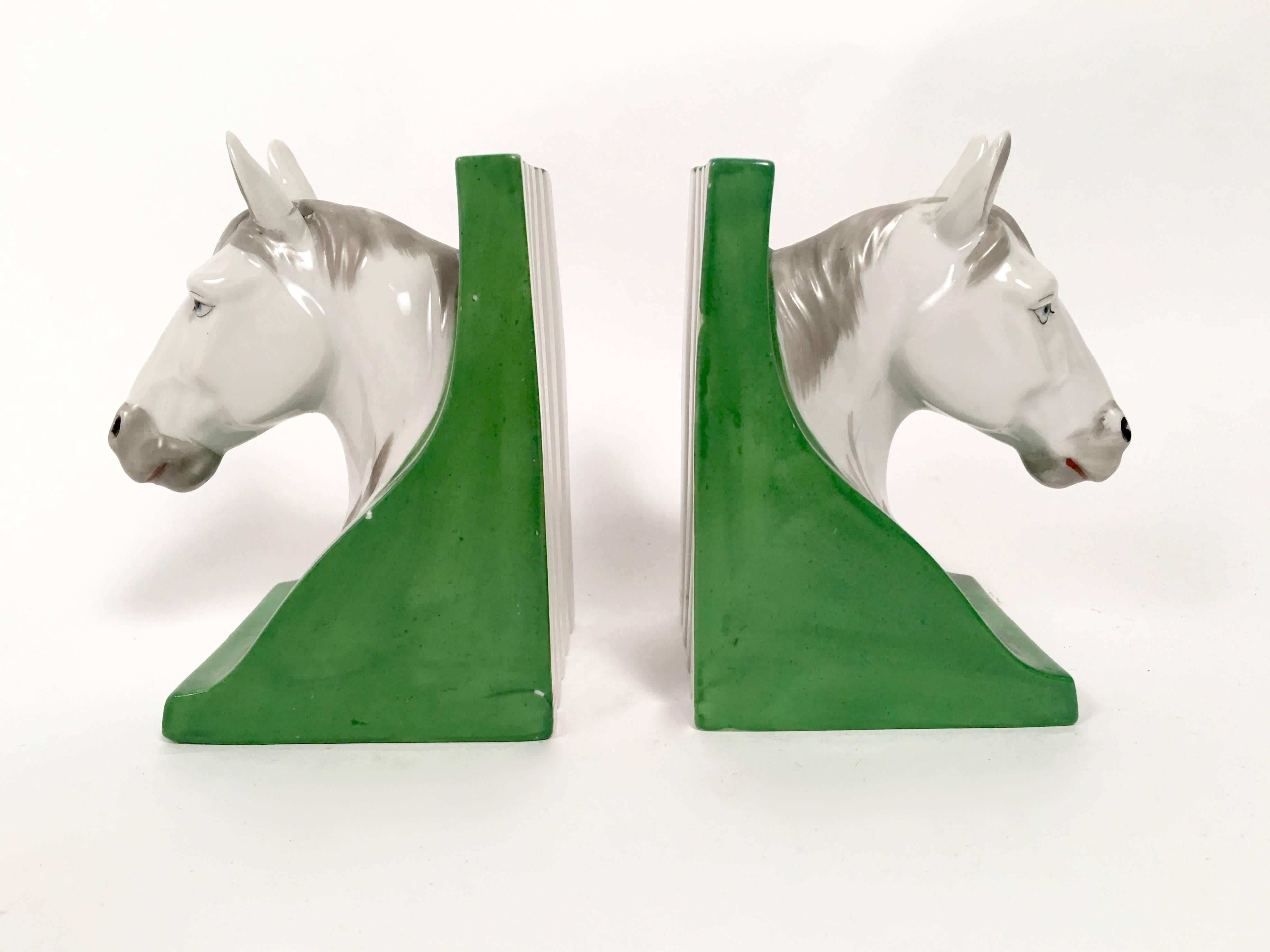 A charming pair of hand-painted ceramic horse head bookends, the expressive white horses with grey manes and blue eyes on emerald green bases.