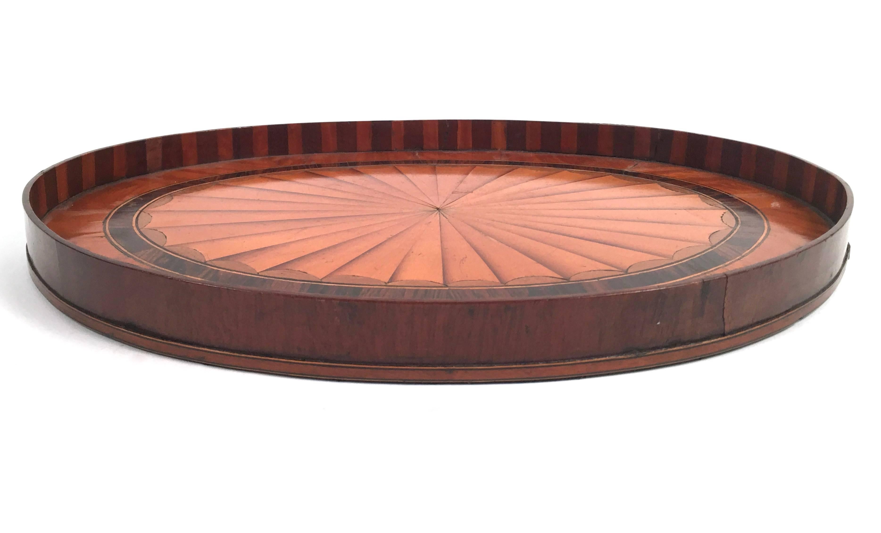A beautifully crafted a and very graphic small Georgian oval tray, with mahogany edge and base, veneered with rosewood, boxwood and satinwood marquetry in the form of a three dimensional circular fan or batwing. The bottom is lined with black felt.