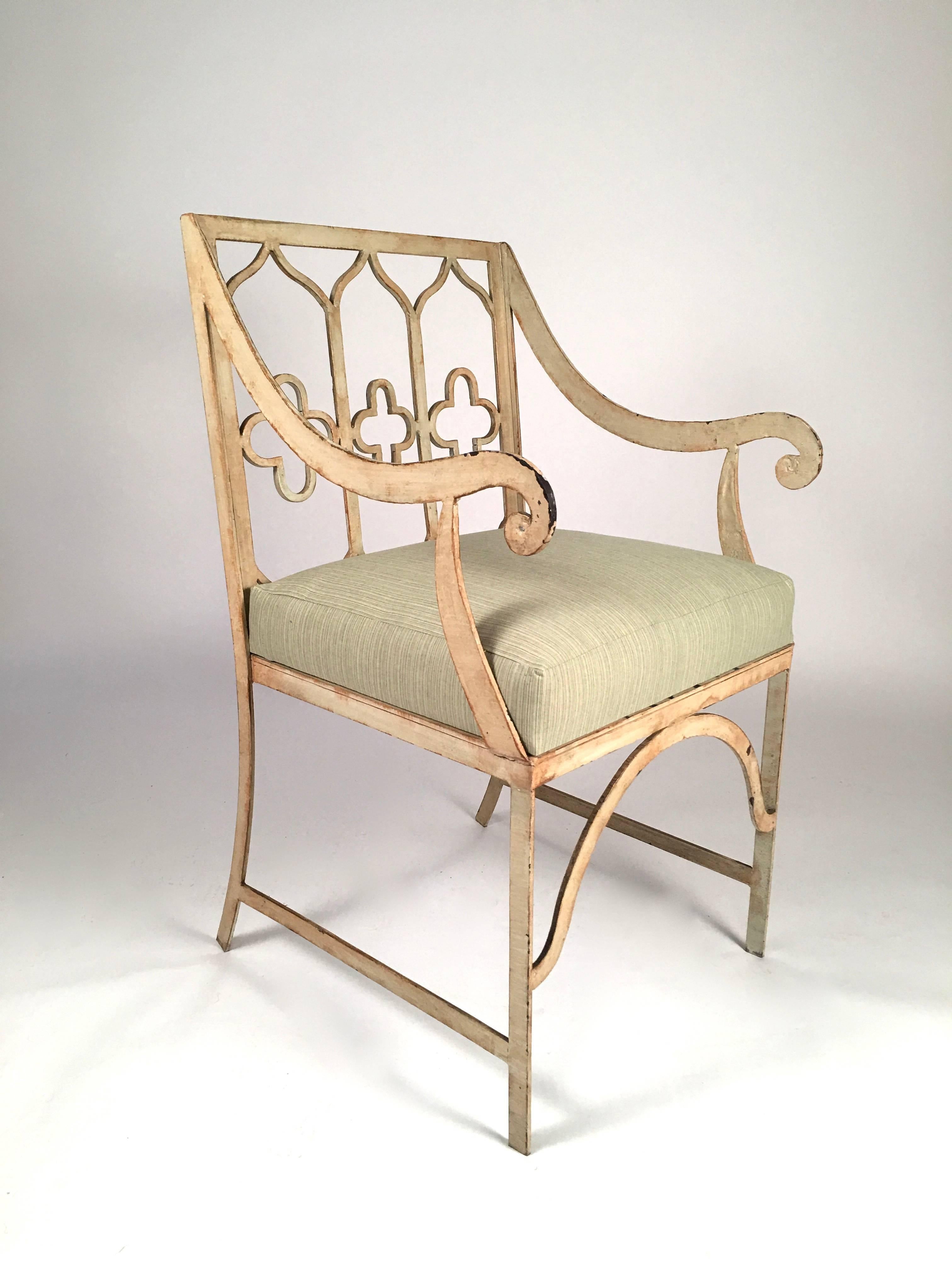 A Gothic Revival garden chair in painted iron, the quake back decorated with gothic tracery and quatrefoils flanked by two down swept scrolling arms over a square, newly upholstered seat with cushion, supported on four legs joined by cross