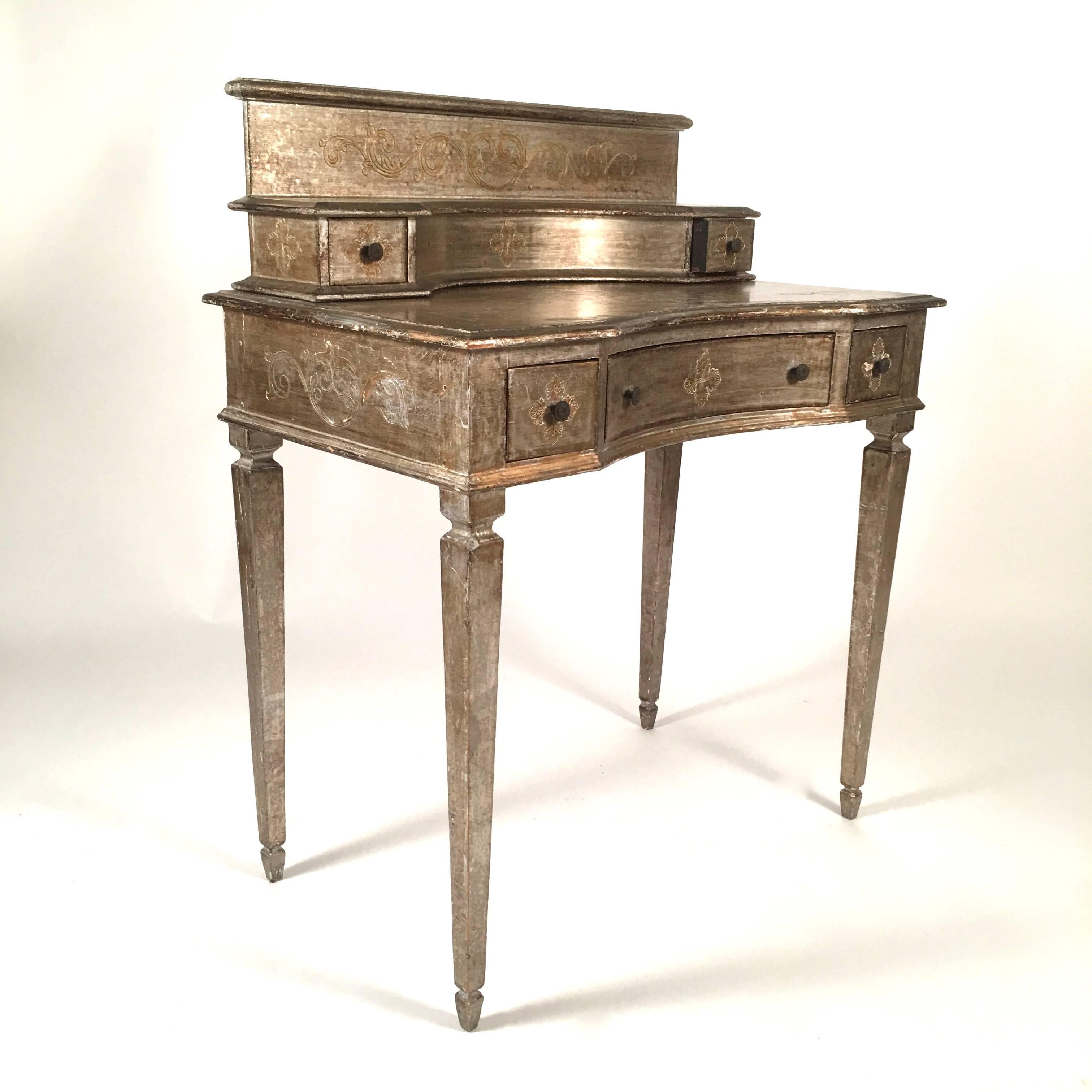 An Italian, likely Florentine, silver leafed dressing or writing table, vanity, the surface decorated with incised scrolled floral and foliate ornament, of rectangular form, the removable superstructure with a gallery top over a semi circular curved
