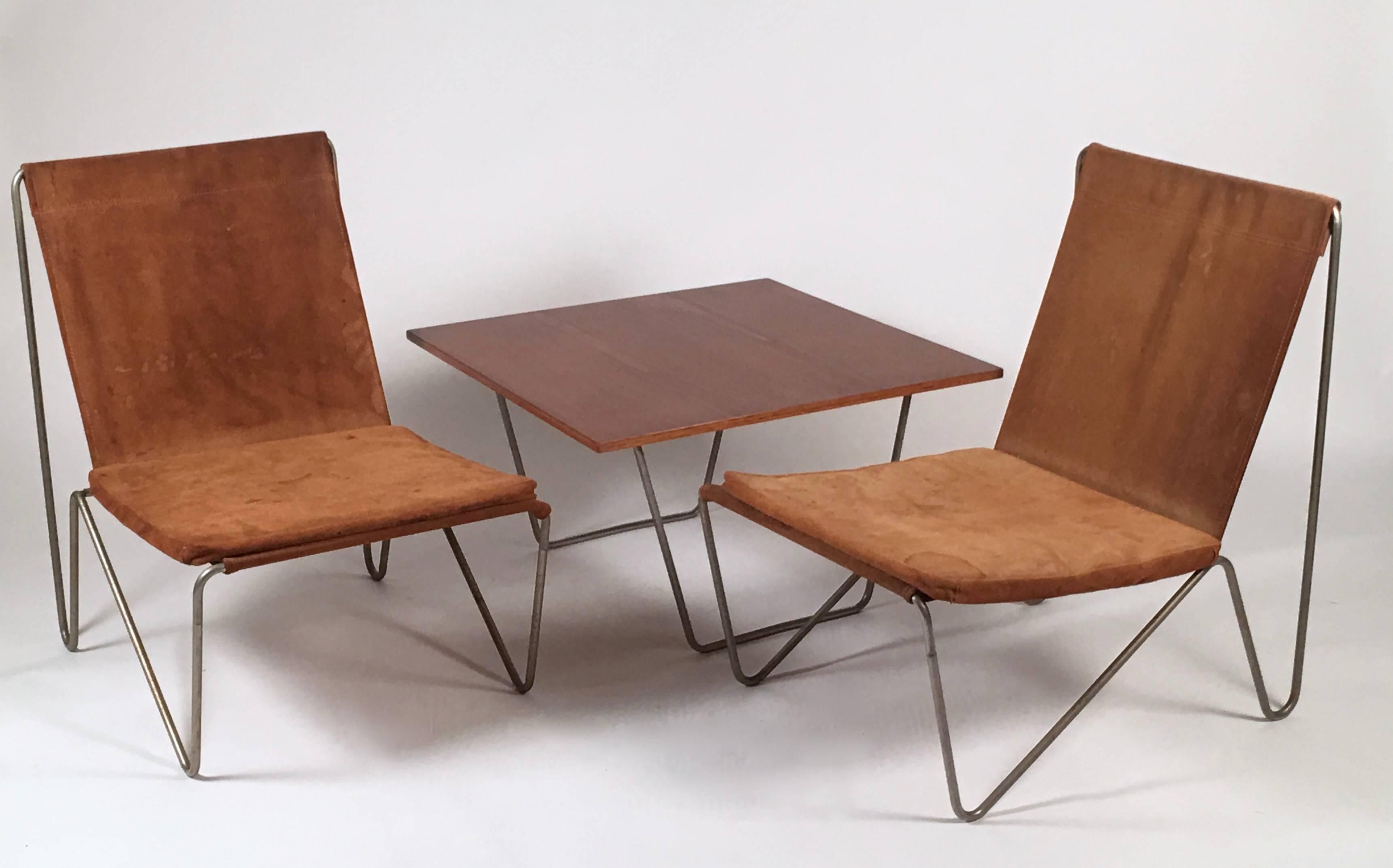 A three-piece set of furniture, comprising a pair of Verner Panton Bachelor chairs, in tubular steel with suede sling seat cushions and upholstery and a teak and steel low table, all made by Fritz Hansen, Danish, circa 1958. Original suede