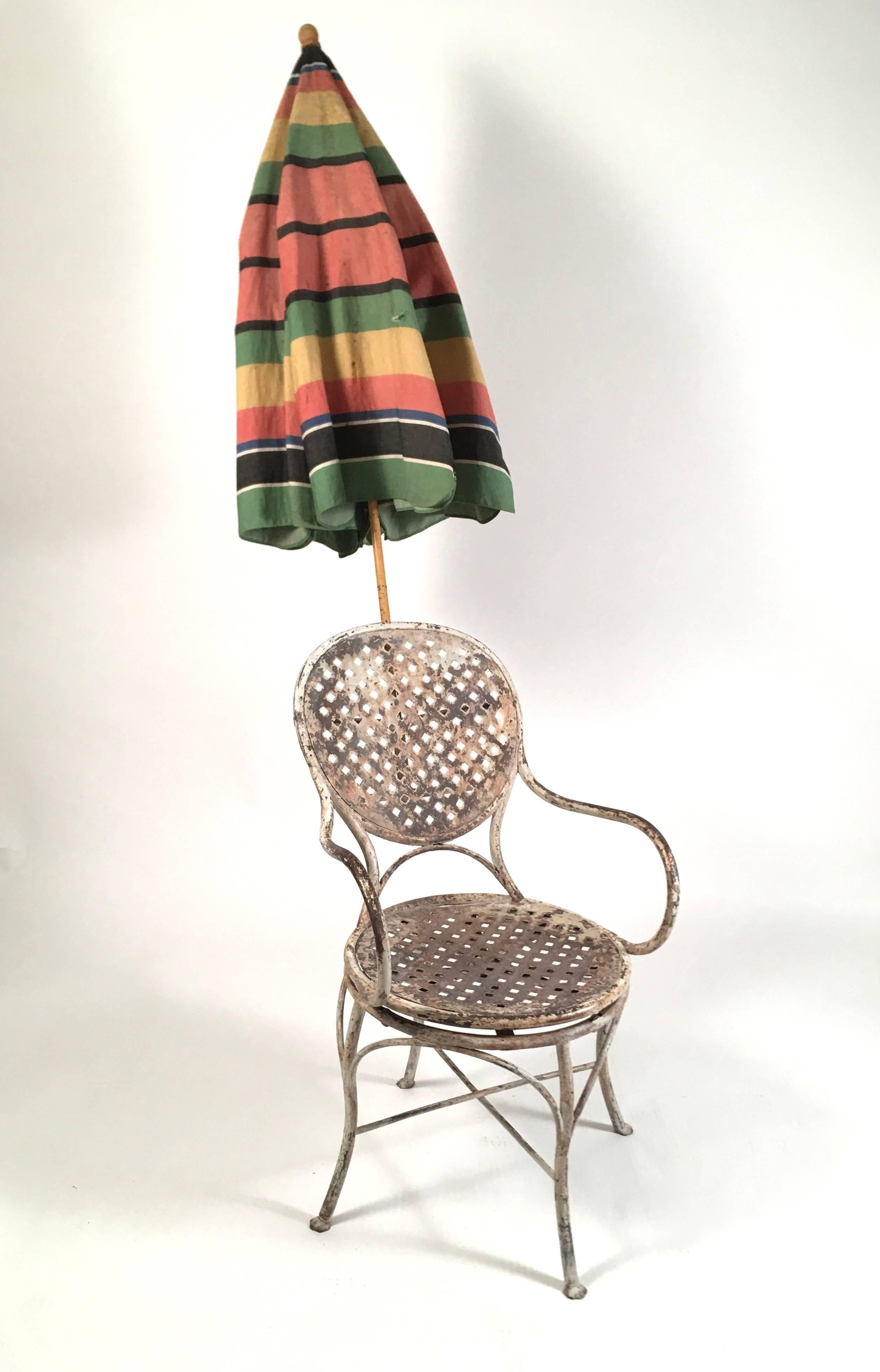 An unusual and wonderful 1920s French painted tubular iron garden chair, with swivel seat and original awning striped umbrella which fits into a cylindrical holder with wing nut on the back of the chair. It is easily added or removed. The seat of