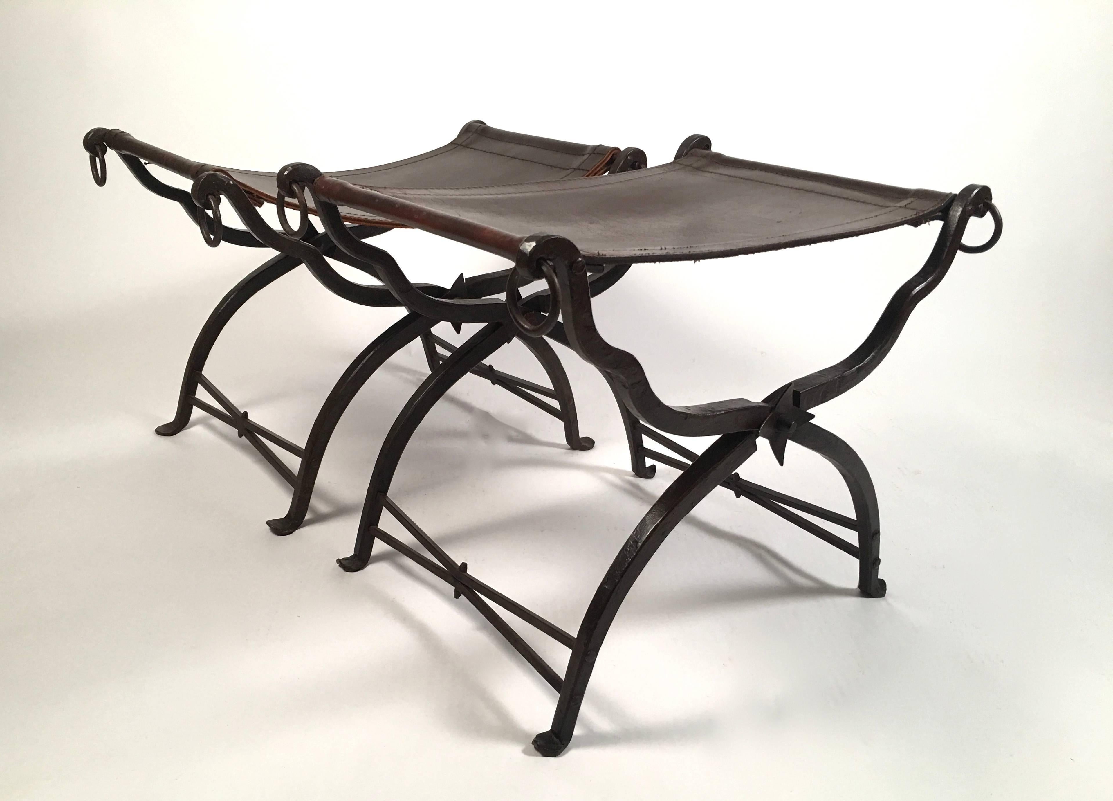 A matched (very similar, but not identical) pair of wrought iron stools or benches with thick leather sling seats, of Curule (an ancient Roman furniture form) or X-shape, by Morgan Colt (1876-1926), a well-known painter and craftsman, who worked in