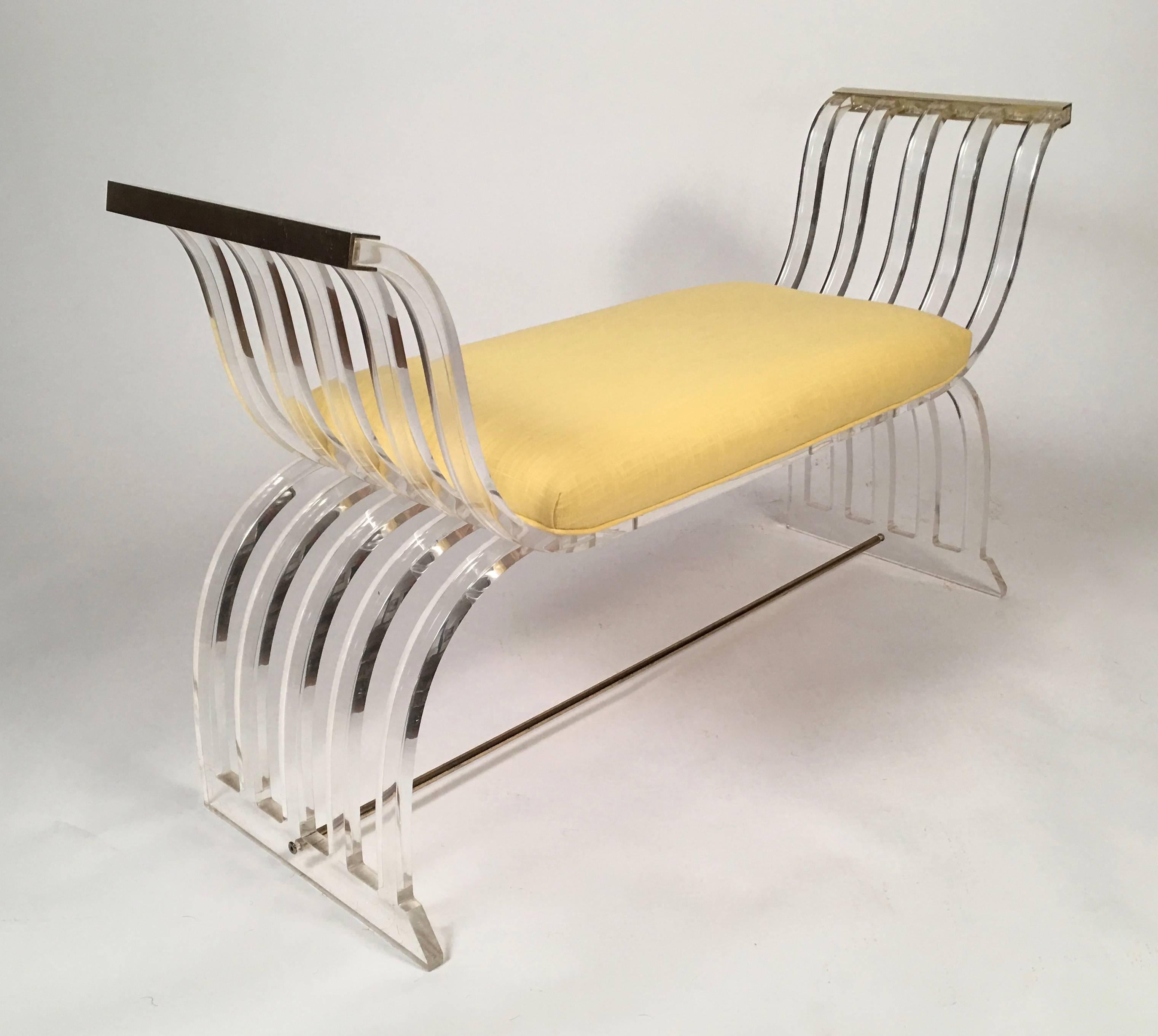 A very well-made vintage lucite and brass bench, in the manner of Charles Hollis Jones, Hollywood Regency style, circa 1960-1970 of neoclassical Curule form, the down swept arm rails capped with brass, with newly upholstered yellow linen seat, over