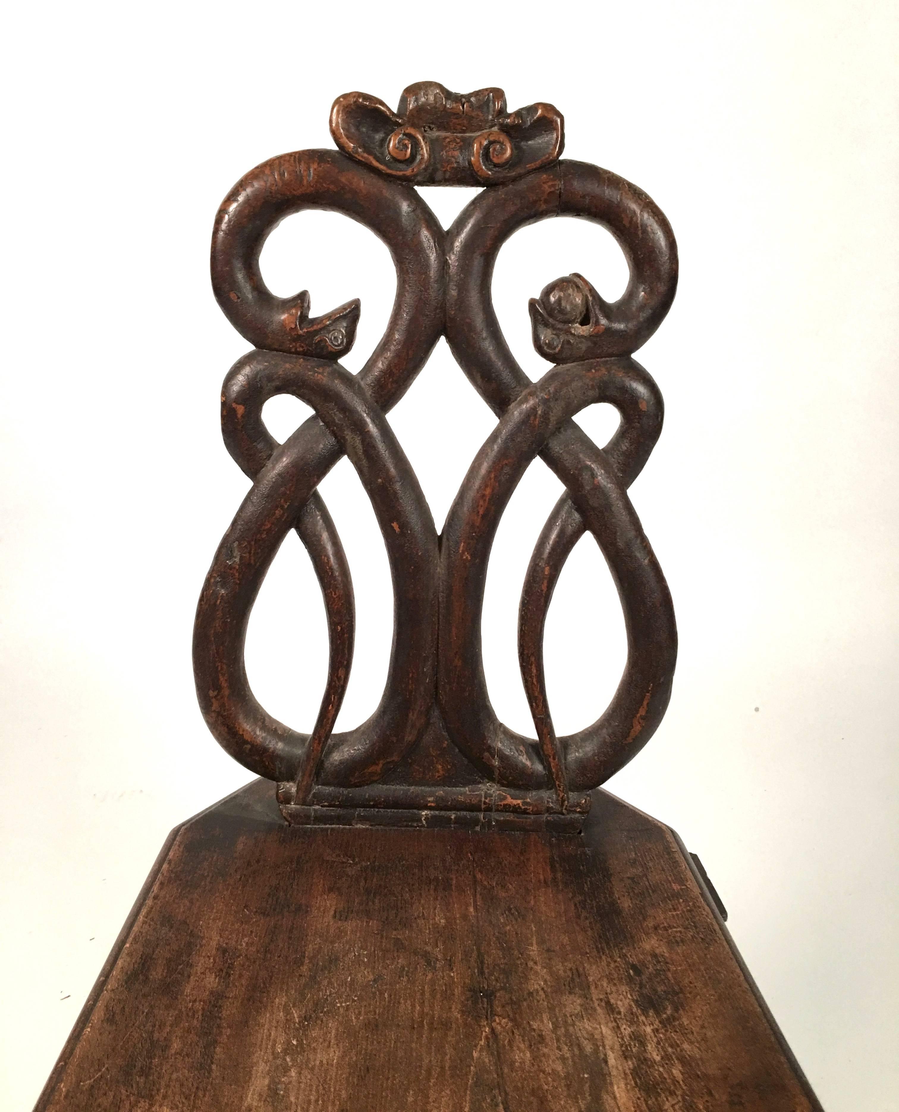 A striking carved walnut Baroque sgabello, or side chair, the back with a carved stylized shell over two intertwined snakes, one with an apple in its mouth, over a rectangular seat with canted corners, supported by four chamfered, splayed legs. The