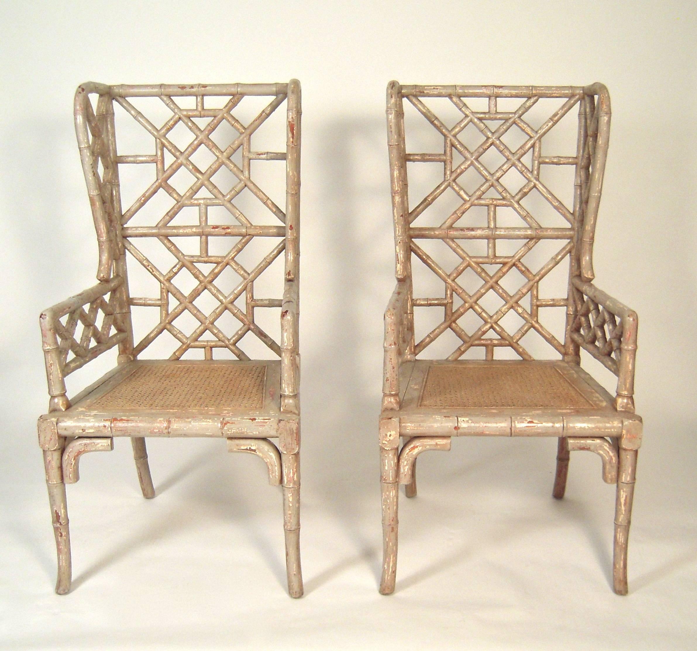 A pair of stylish chinoiserie faux bamboo wing chairs, beautifully crafted of carved wood to resemble bamboo, in a distressed painted finish. Very comfortable.