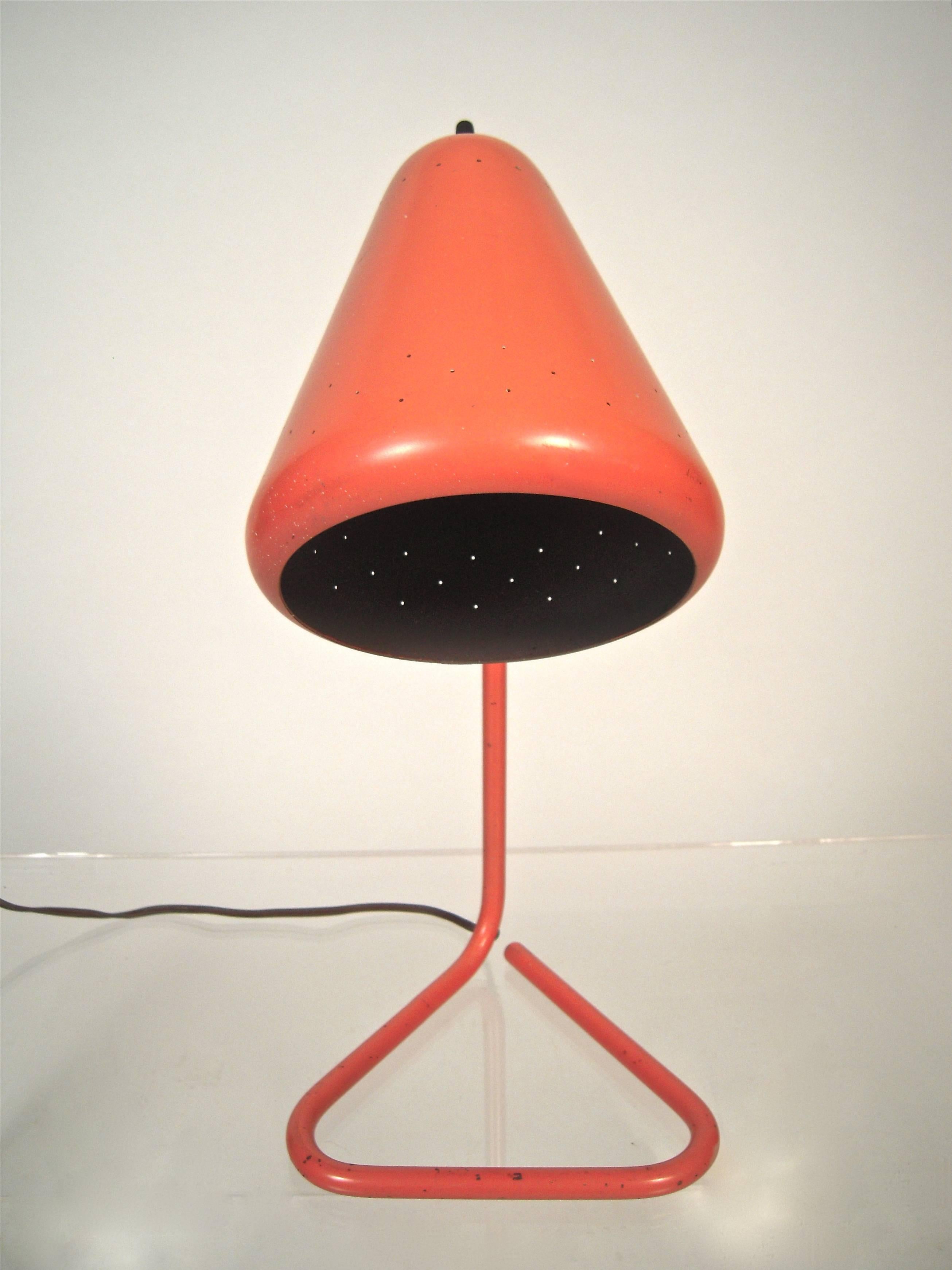 An adjustable desk lamp by Kurt Versen (1901-1997) in a beautiful coral color, American, circa 1950, the conical shade, perforated with three rows of small decorative circles to let light through, which can move up or down, supported by a tubular