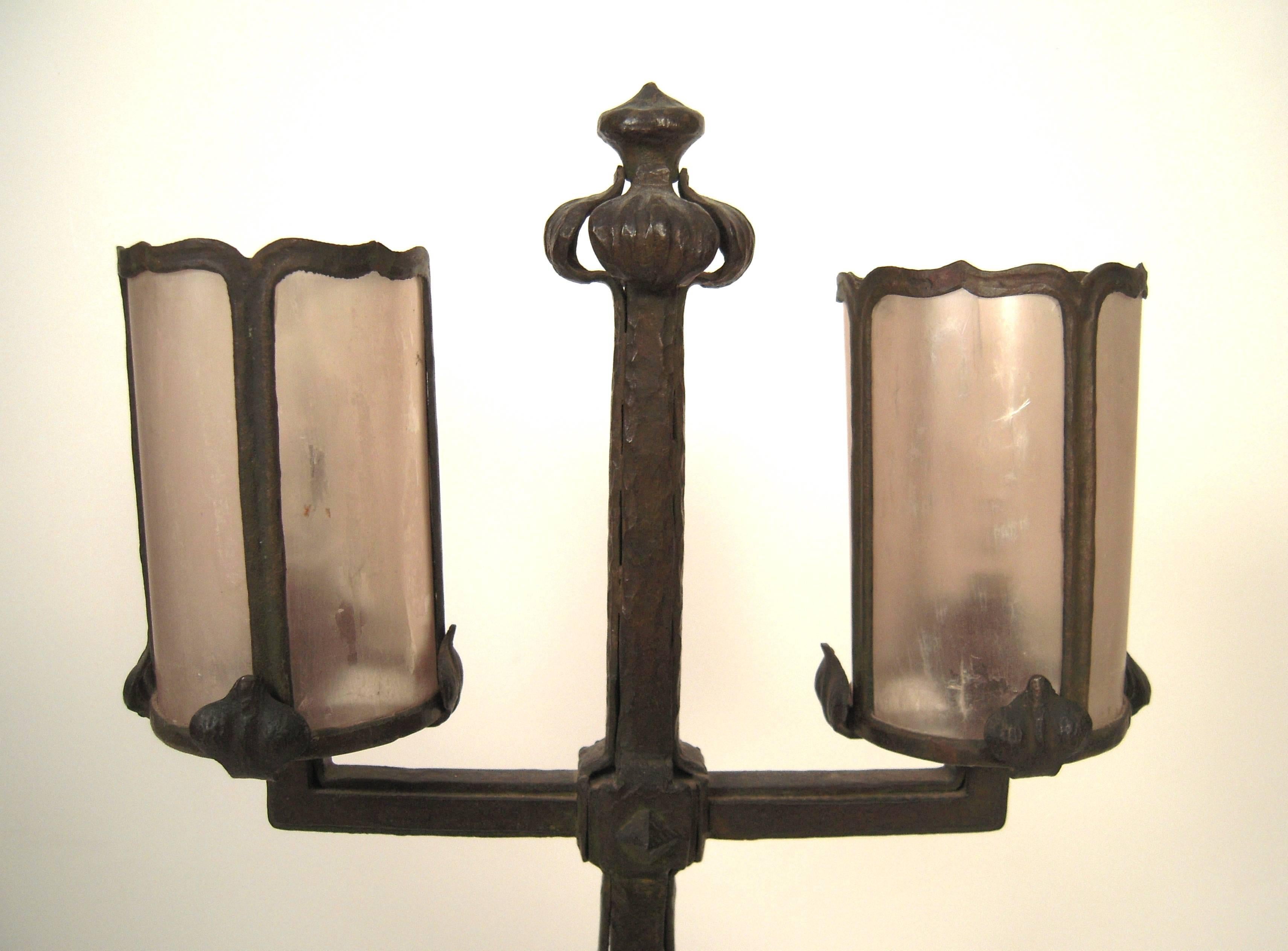 A fine quality Arts and Crafts period wrought iron lamp with its original mica cylindrical shades, supported by leaf-form brackets, on an base formed by four hand-wrought straps, terminating in a leaf or flower-form base, circa 1905. Wonderful