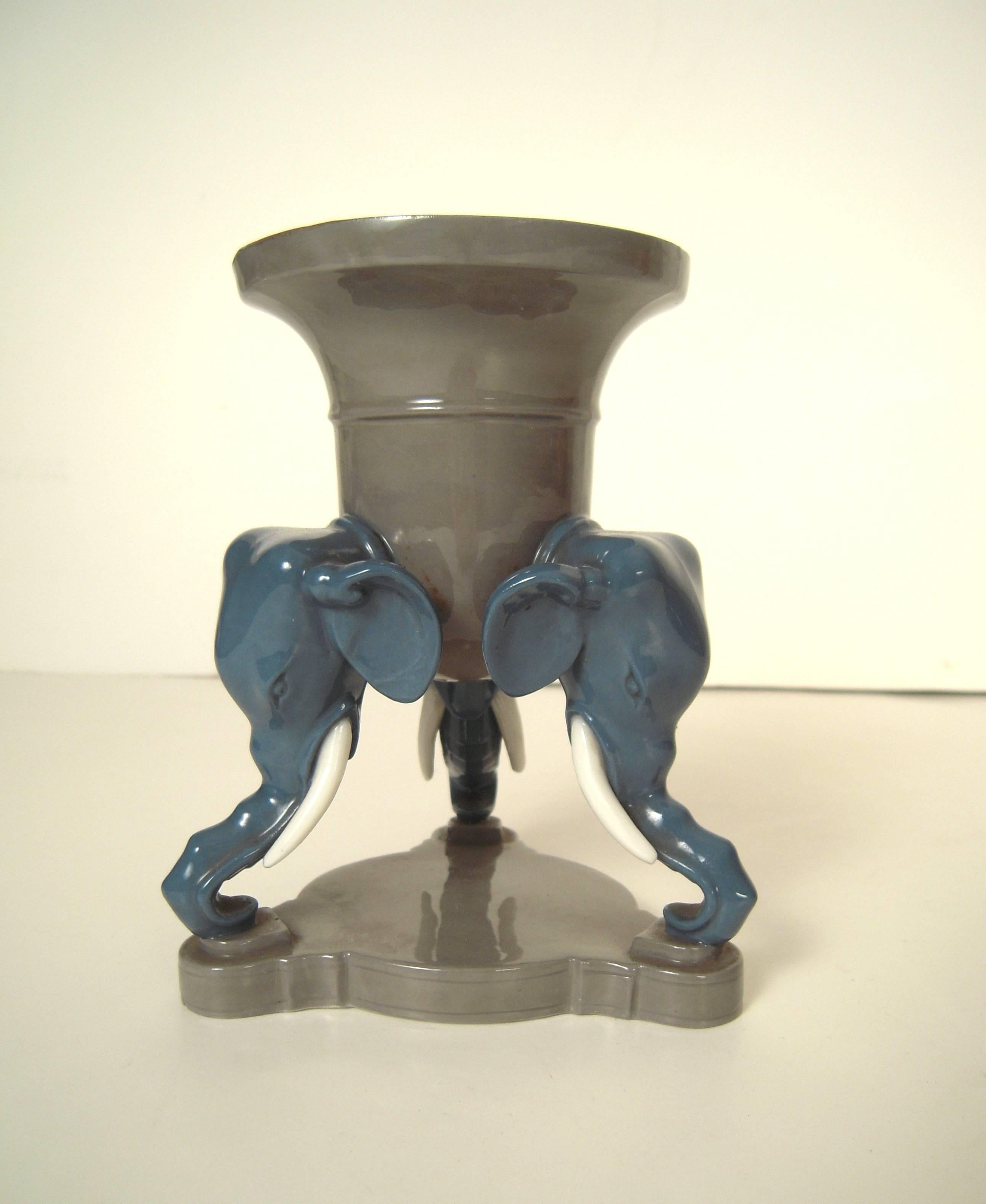 A well modeled ceramic vase, English, circa 1875, in the form of an inverted bell shaped vessel, glazed in sage green, supported by three blue elephant heads with white tusks, on a shaped triangular plinth, with impressed 'Mintons' mark on the