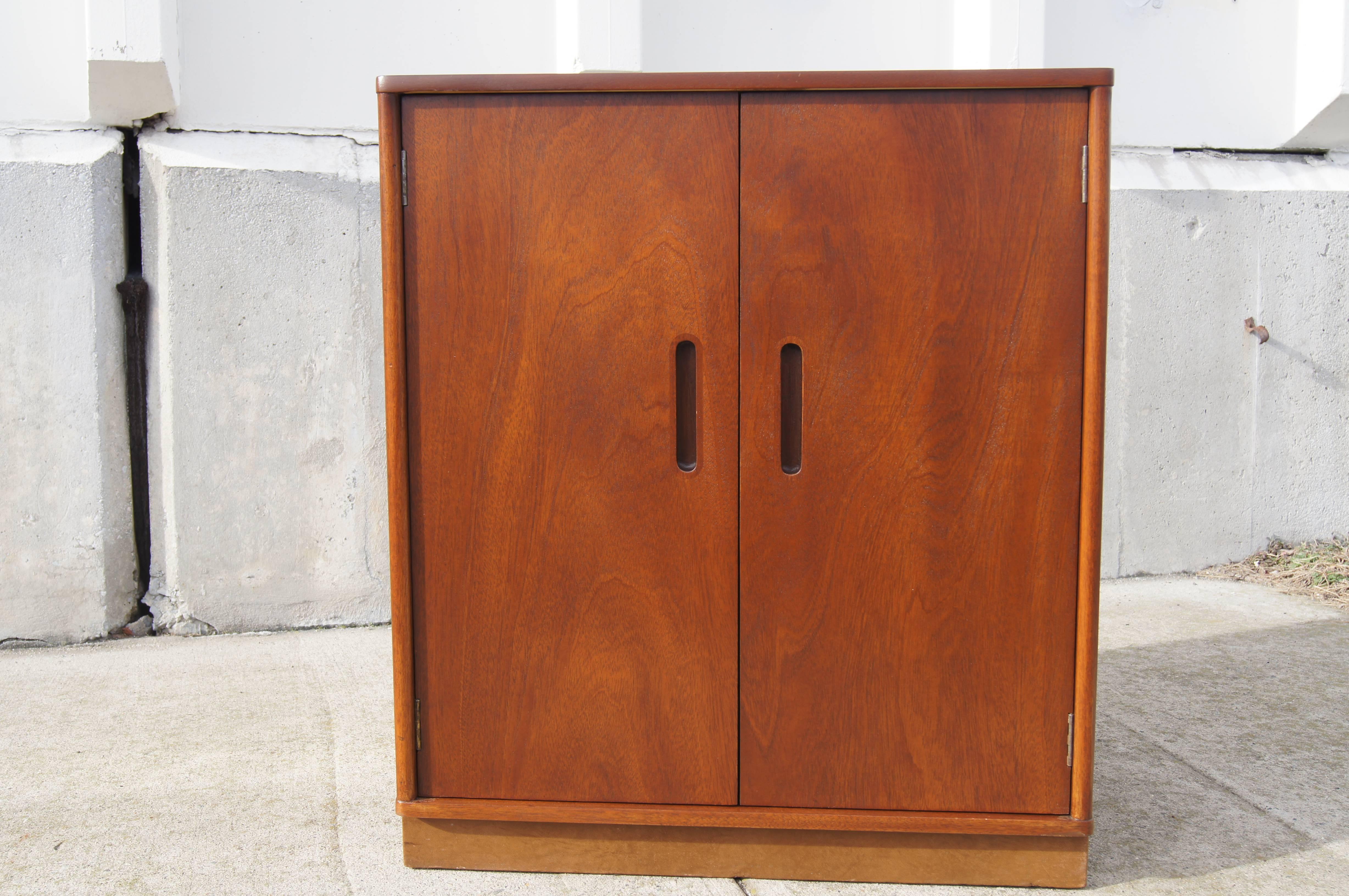 Designed by Edward Wormley for Dunbar, this trim mid-century cabinet in walnut-stained mahogany features recessed door pulls and a matching leather-wrapped base. Inside are two adjustable shelves.