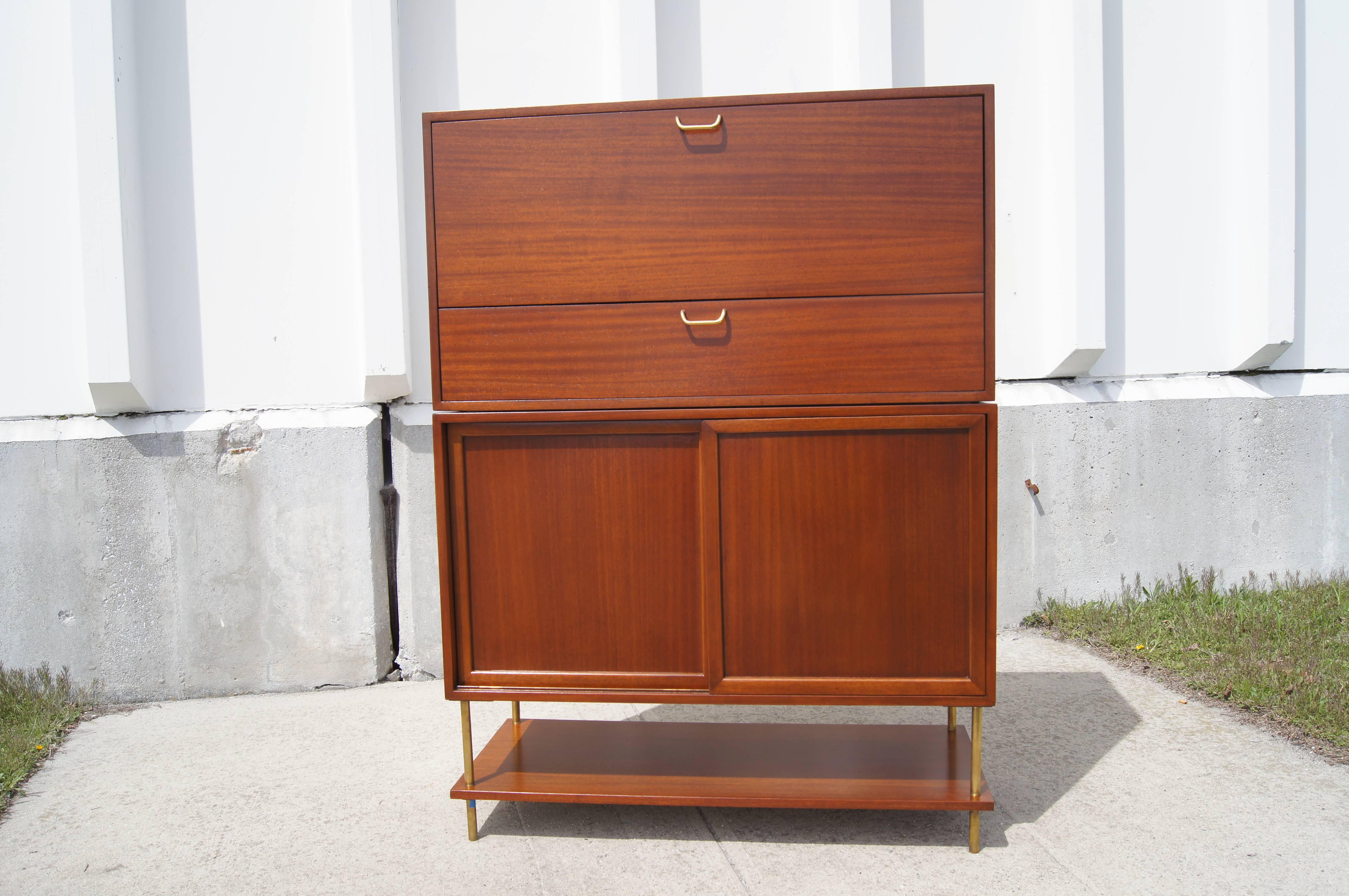 This mahogany and brass bar cabinet by Harvey Probber provides ample storage. The top of the cabinet hinges open to reveal a small laminate drawer and serving space. The lower cabinet has three laminate drawers and an adjustable shelf. Below is an
