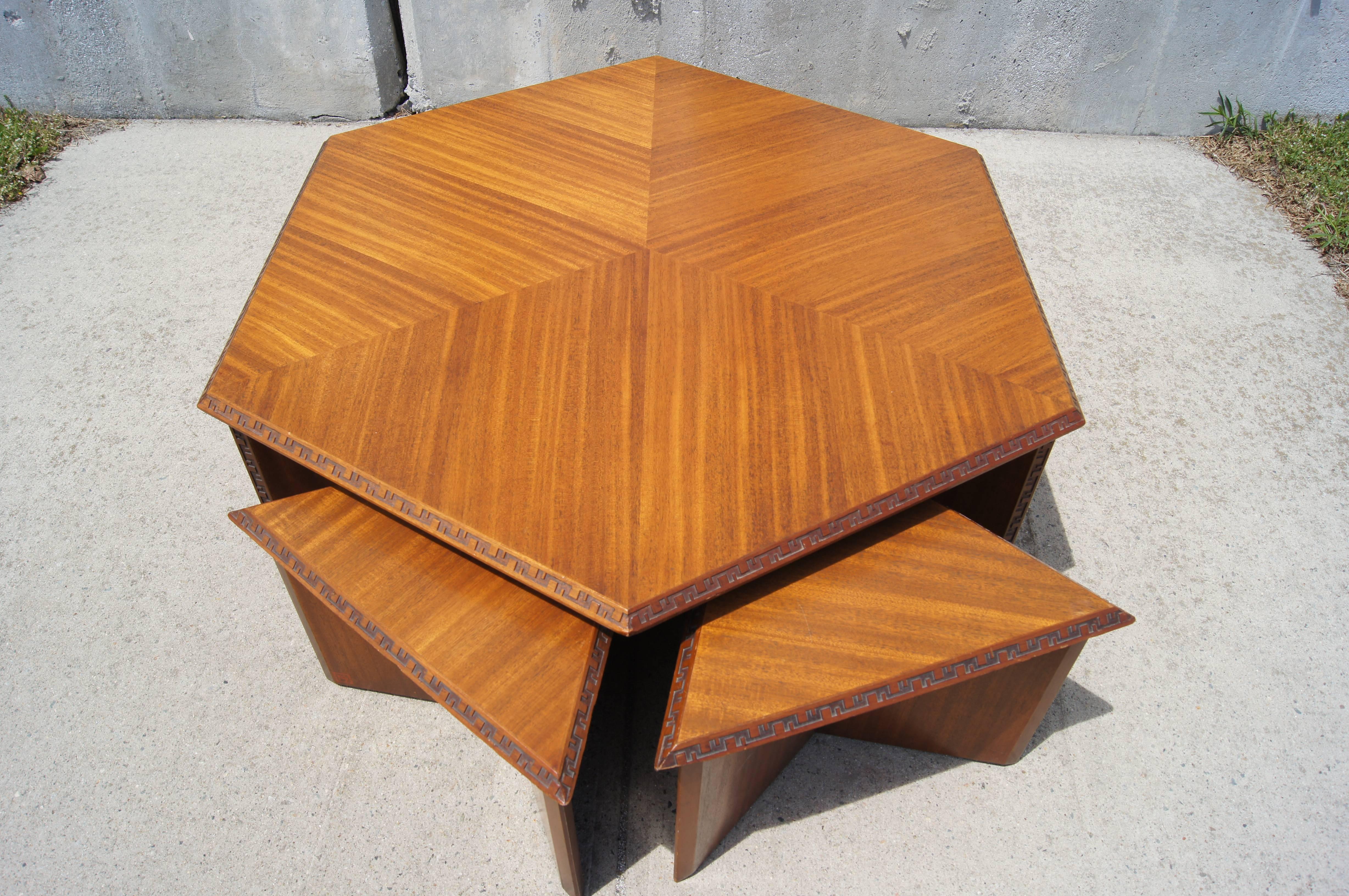 This handsome set is part of the Taliesin collection that Frank Lloyd Wright designed for Henredon in 1955. It comprises a coffee table whose hexagonal top sits on a tripod base and two triangular stools that fit underneath. 

The solid mahogany