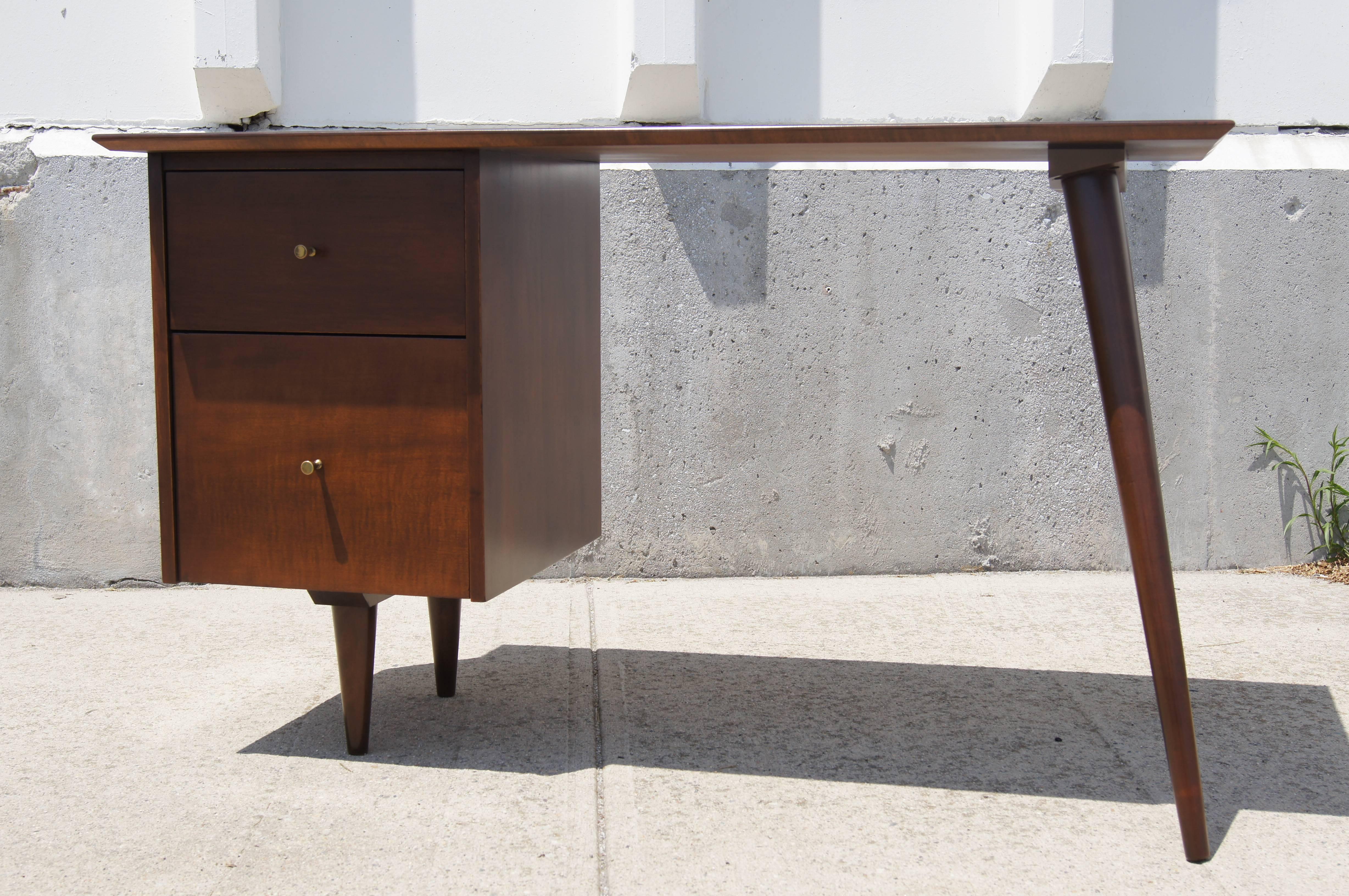 Part of the Planner Group that Paul McCobb designed for Winchendon in the 1950s, this classic desk places a rectangular top over a bank of two drawers on the left and two tapered dowel legs canted to the right. The solid maple desk is finished with