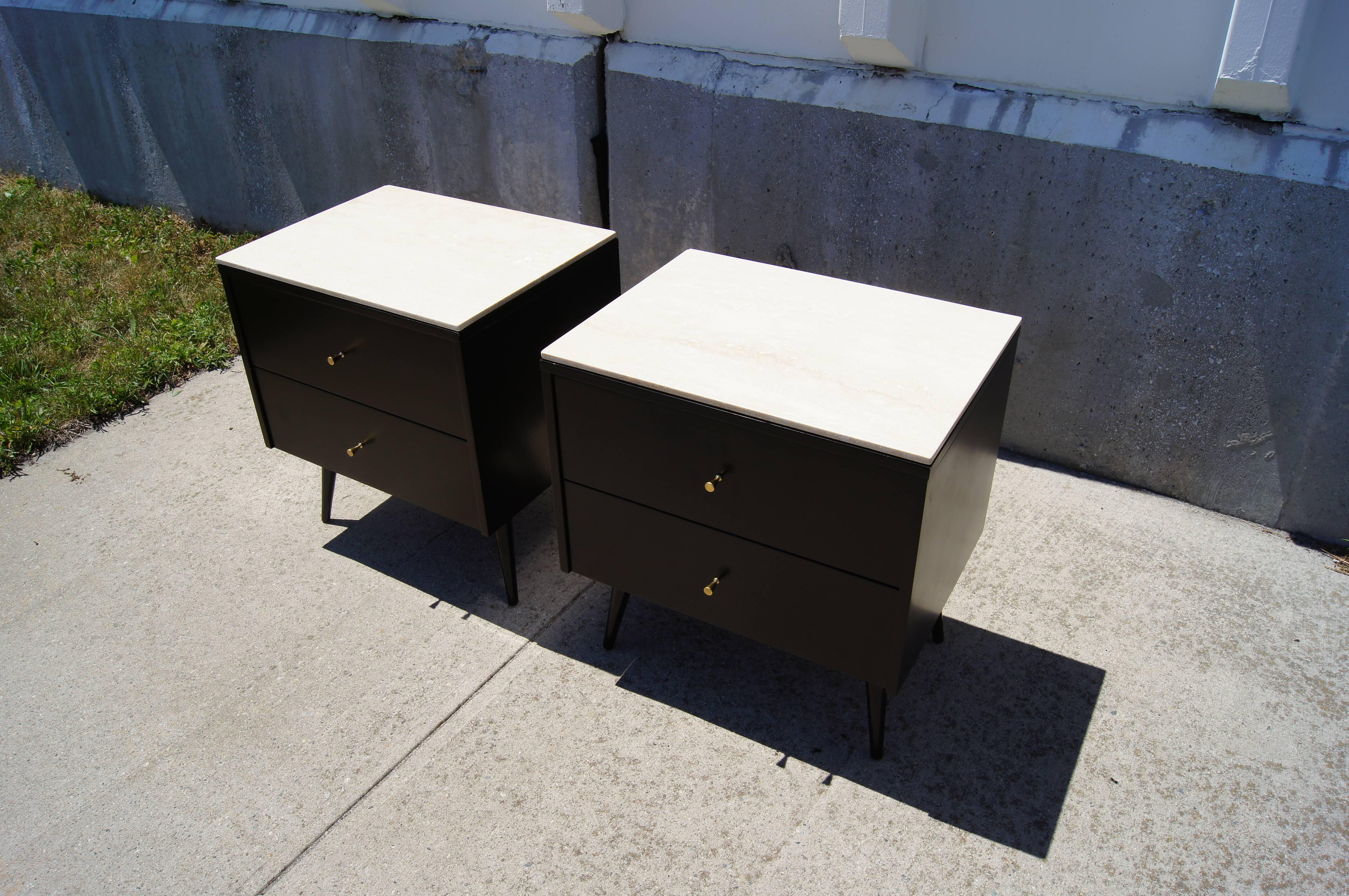 Part of Paul McCobb’s Planner group for Winchendon, this pair of nightstands comprises black-lacquered maple cases with two drawers set on canted legs. The contrasting white travertine marble tops and brass conical pulls make them an especially