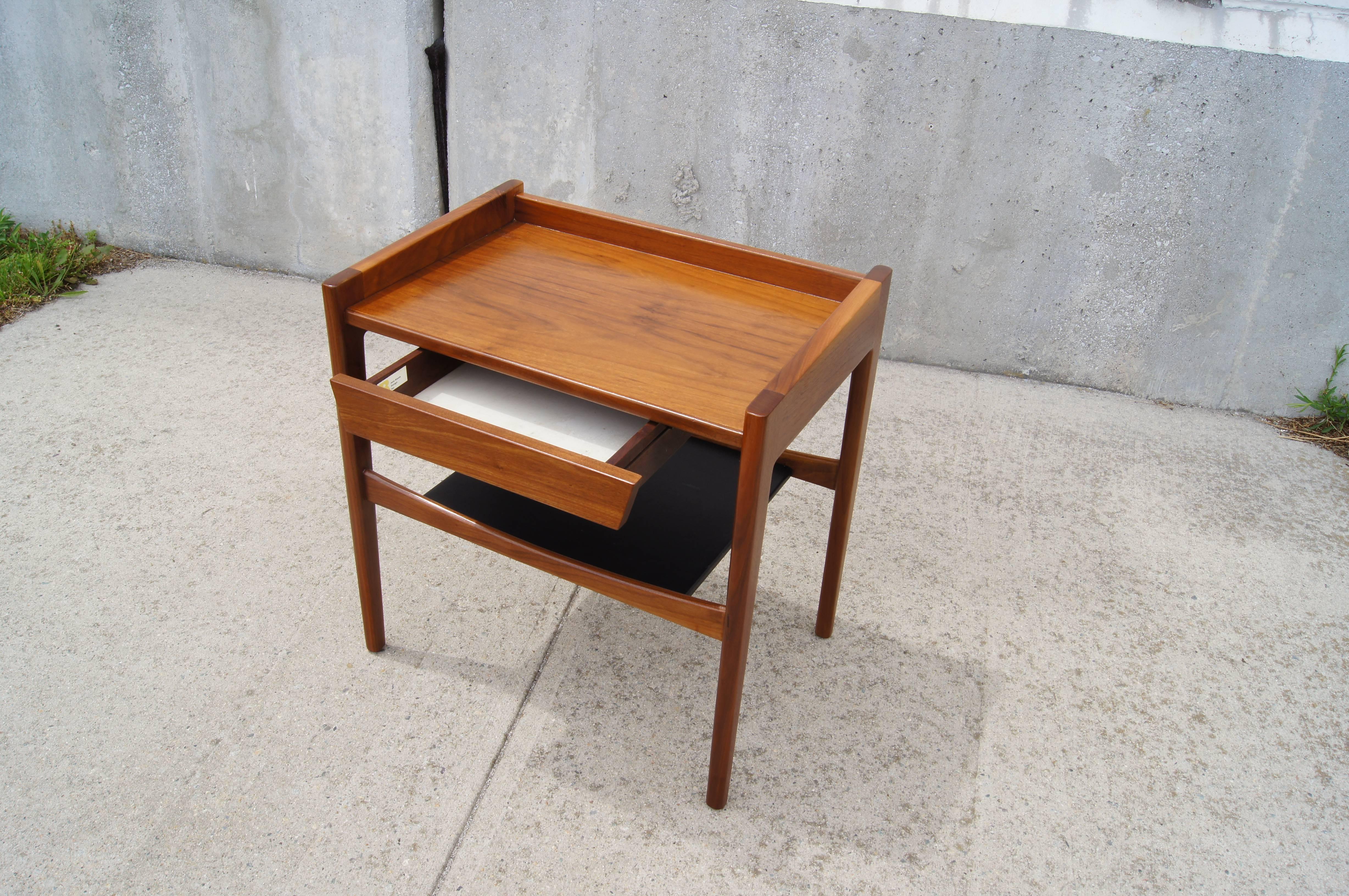 Jens Risom designed this distinctive walnut side table with a raised gallery on three sides, a single suspended drawer and a low shelf covered in black leather. A rarely seen piece with great charm.